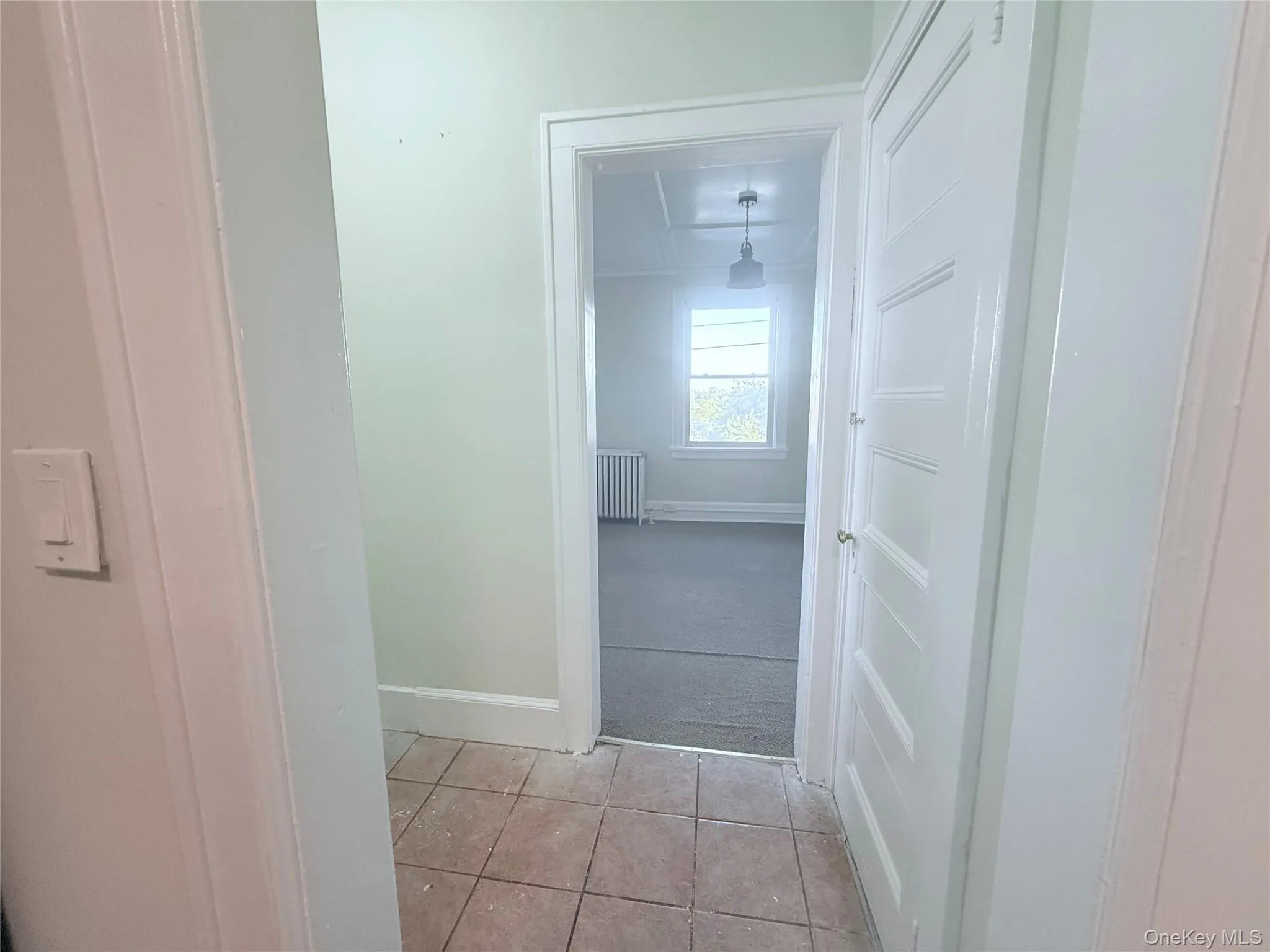 Hallway with light tile patterned floors, light carpet, and radiator heating unit Hallway with light tile patterned floors, light carpet, and radiator heating unit