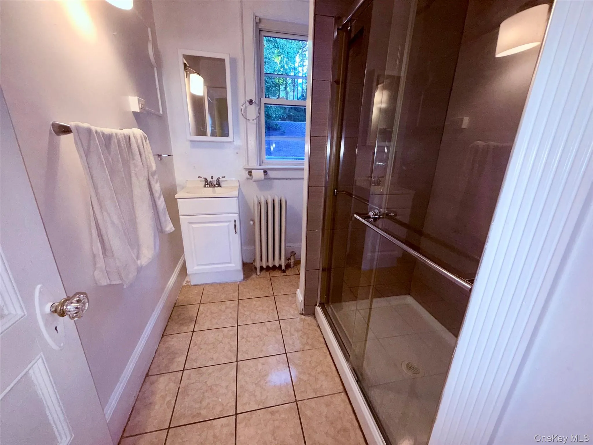 Bathroom with vanity, light tile patterned flooring, a stall shower, and radiator Bathroom with vanity, light tile patterned flooring, a stall shower, and radiator