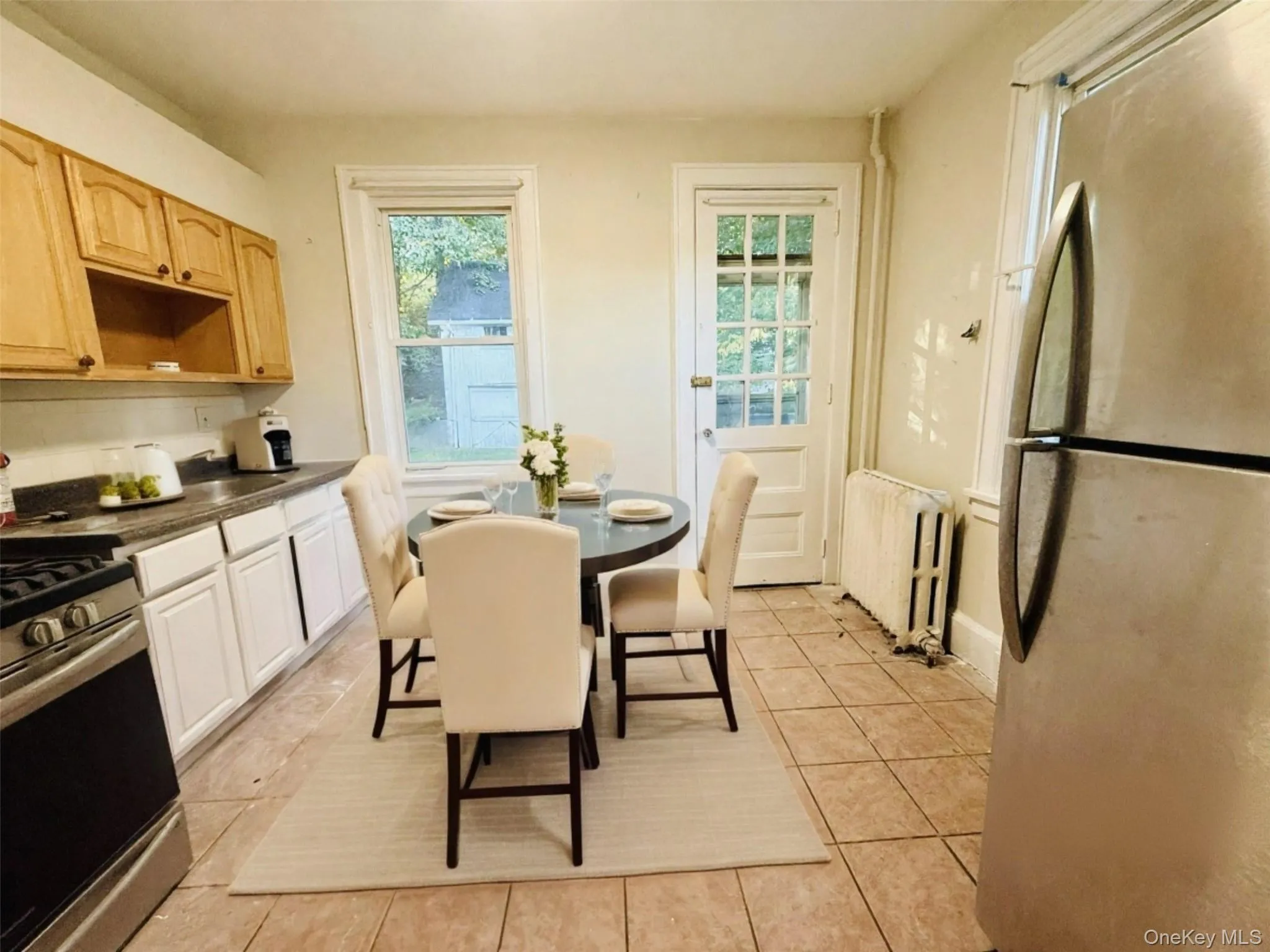 Kitchen featuring stainless steel appliances, dark countertops, radiator heating unit, and light tile patterned floors Kitchen featuring stainless steel appliances, dark countertops, radiator heating unit, and light tile patterned floors