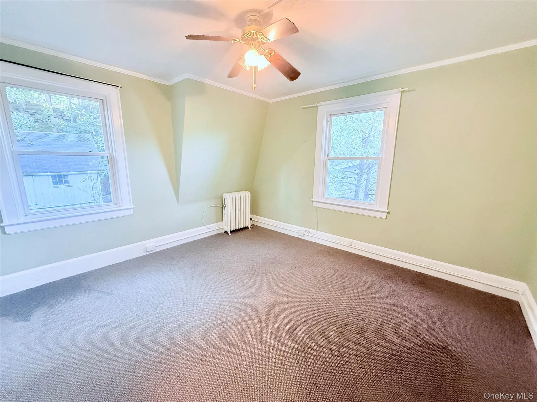 Carpeted spare room with ornamental molding, radiator, and a ceiling fan Carpeted spare room with ornamental molding, radiator, and a ceiling fan