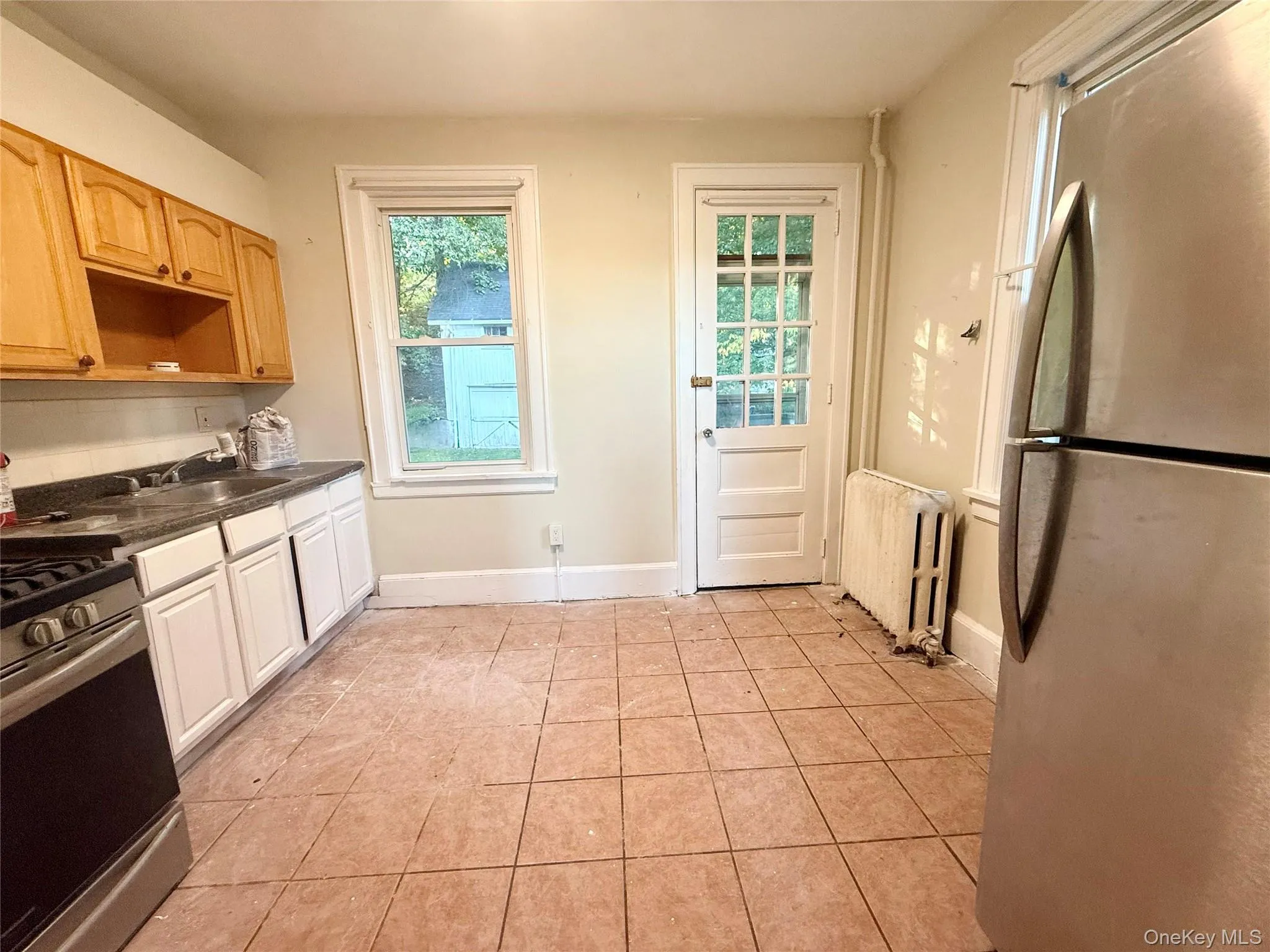 Kitchen featuring stainless steel appliances, dark countertops, light tile patterned floors, and radiator Kitchen featuring stainless steel appliances, dark countertops, light tile patterned floors, and radiator