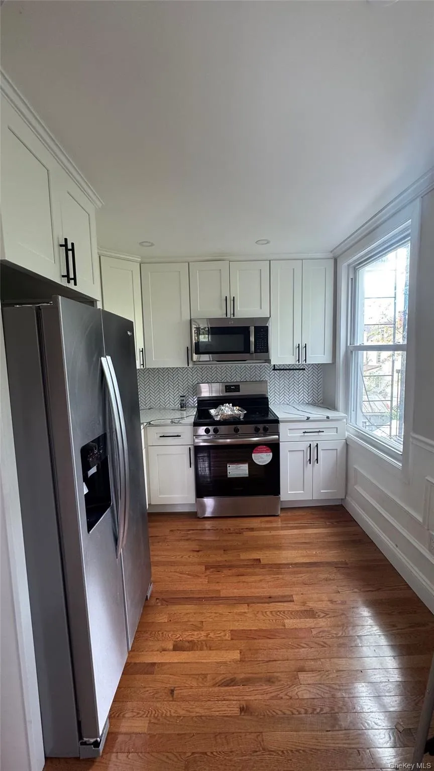 Kitchen with white cabinets, appliances with stainless steel finishes, tasteful backsplash, dark wood finished floors, and light stone countertops Kitchen with white cabinets, appliances with stainless steel finishes, tasteful backsplash, dark wood finished floors, and light stone countertops