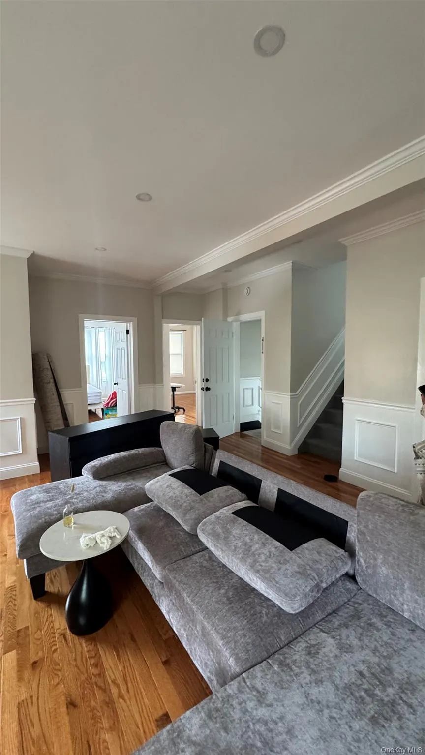 Living room featuring a wainscoted wall, a decorative wall, crown molding, wood finished floors, and stairs Living room featuring a wainscoted wall, a decorative wall, crown molding, wood finished floors, and stairs