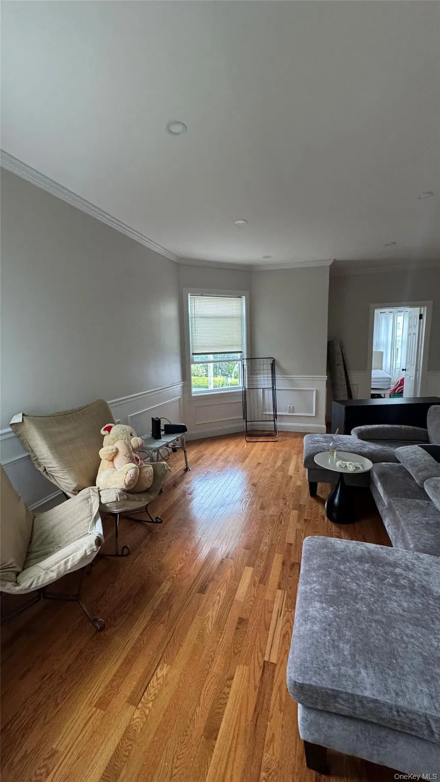 Living room featuring crown molding, wainscoting, light wood-style flooring, and a decorative wall Living room featuring crown molding, wainscoting, light wood-style flooring, and a decorative wall