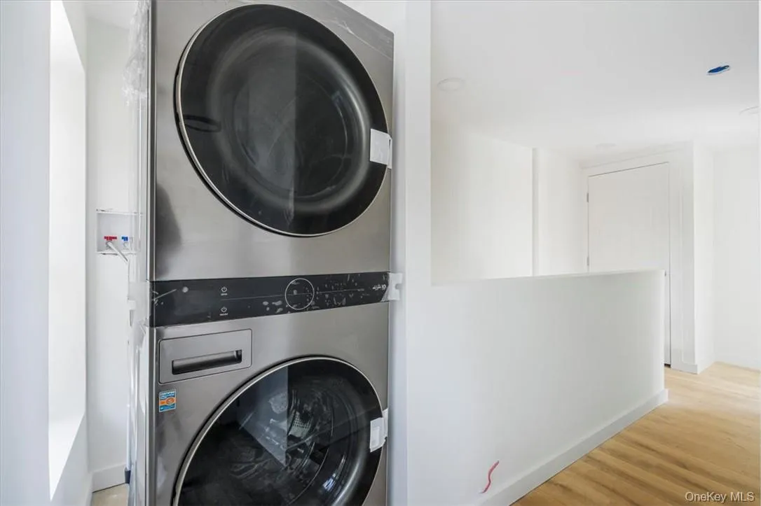 Laundry area featuring stacked washer / dryer and light wood-style floors Laundry area featuring stacked washer / dryer and light wood-style floors