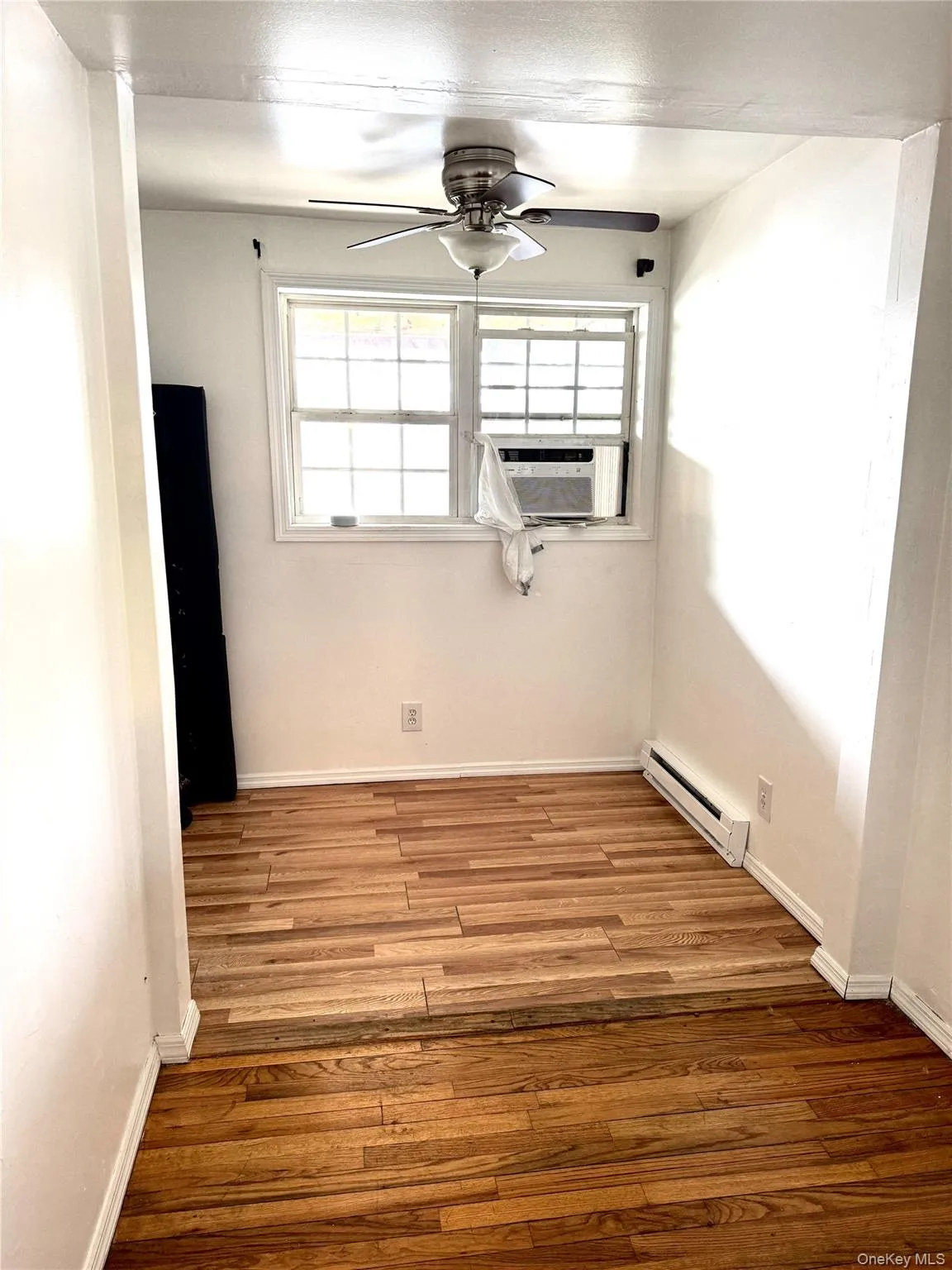 Unfurnished room featuring a baseboard heating unit, ceiling fan, wood finished floors, and plenty of natural light Unfurnished room featuring a baseboard heating unit, ceiling fan, wood finished floors, and plenty of natural light