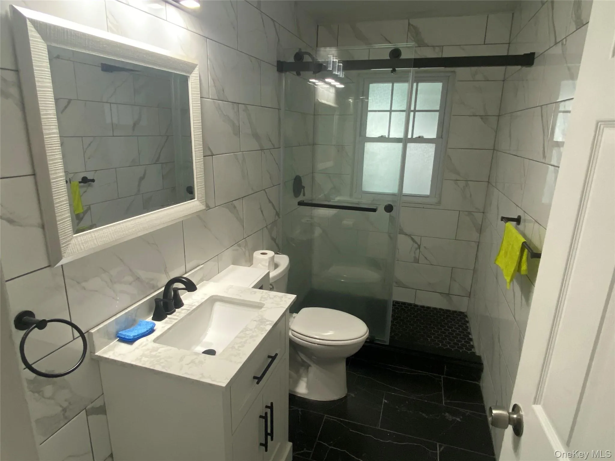 Full bathroom featuring tile walls, vanity, a shower stall, dark marble finish flooring, and tasteful backsplash Full bathroom featuring tile walls, vanity, a shower stall, dark marble finish flooring, and tasteful backsplash