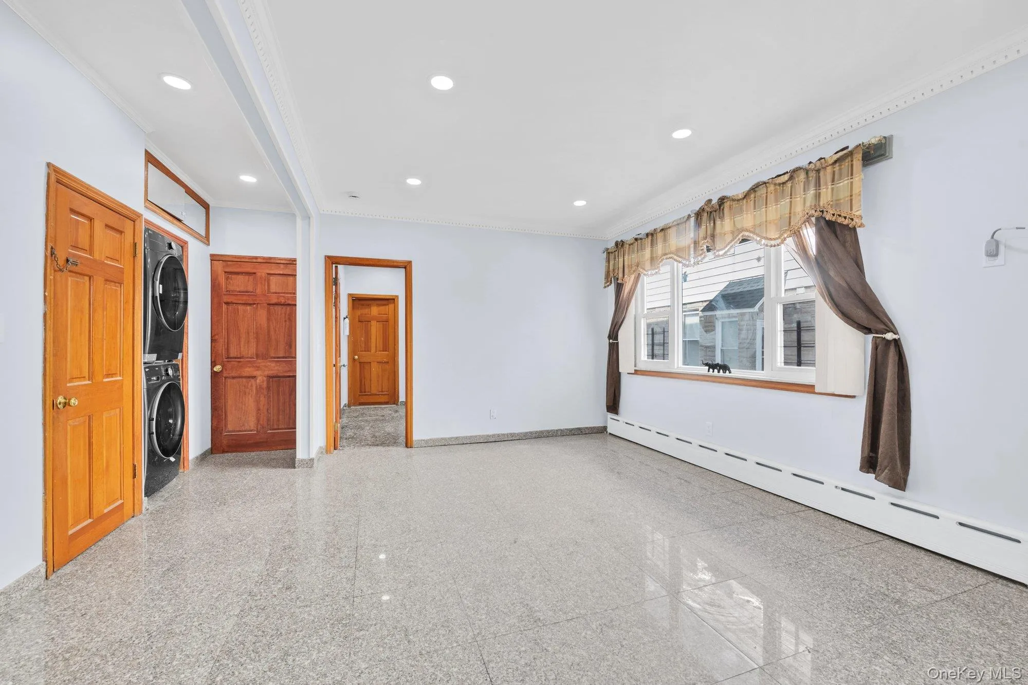 Spare room with granite tiled floors, crown molding, stacked washer / drying machine, recessed lighting, and a baseboard radiator Spare room with granite tiled floors, crown molding, stacked washer / drying machine, recessed lighting, and a baseboard radiator