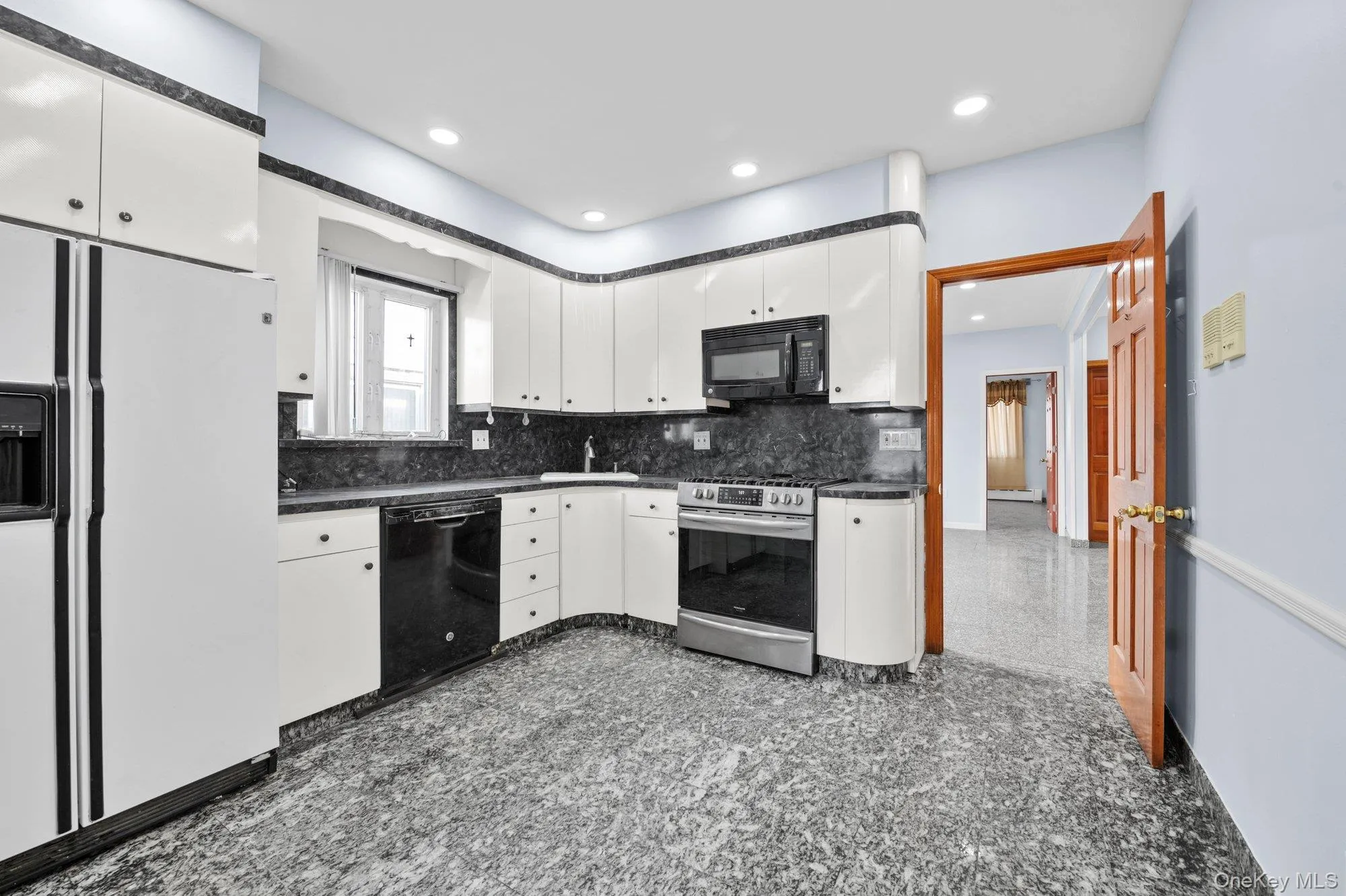 Kitchen with dark countertops, black appliances, white cabinetry, granite tiled floors, and decorative backsplash Kitchen with dark countertops, black appliances, white cabinetry, granite tiled floors, and decorative backsplash