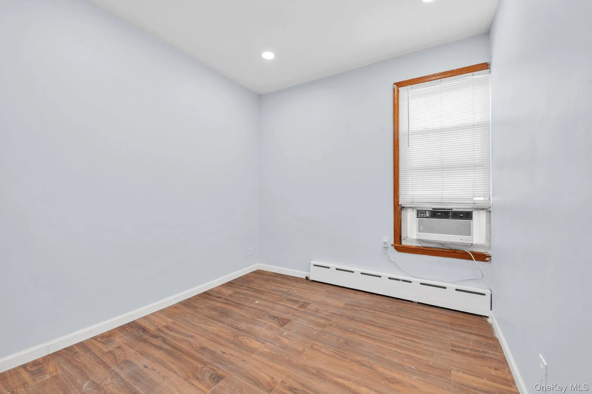 Empty room with baseboard heating, wood finished floors, recessed lighting, and cooling unit Empty room with baseboard heating, wood finished floors, recessed lighting, and cooling unit