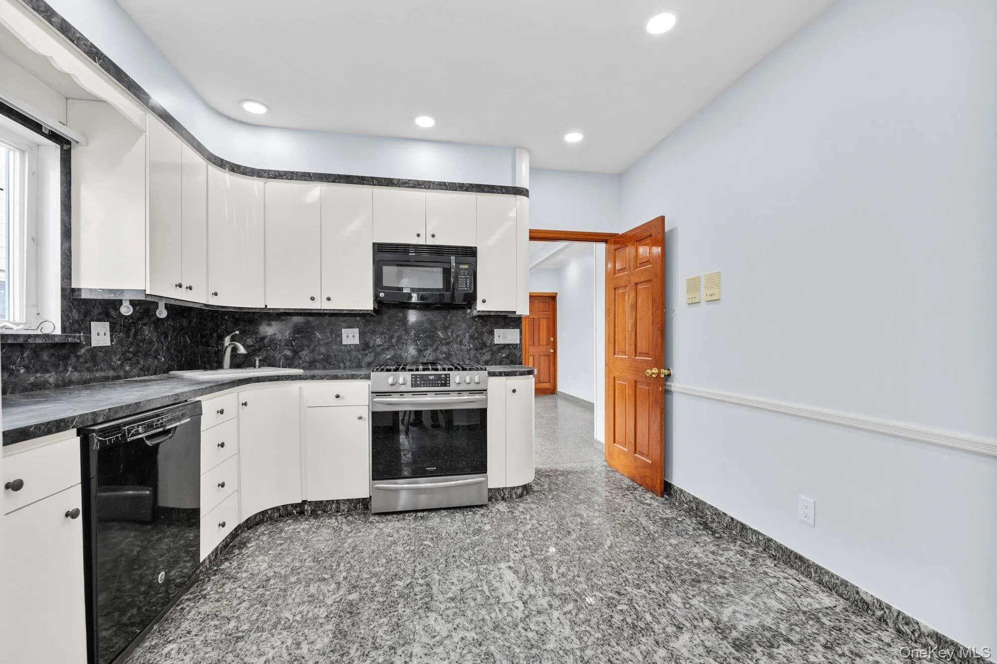 Kitchen featuring dark countertops, decorative backsplash, black appliances, white cabinets, and granite floors Kitchen featuring dark countertops, decorative backsplash, black appliances, white cabinets, and granite floors