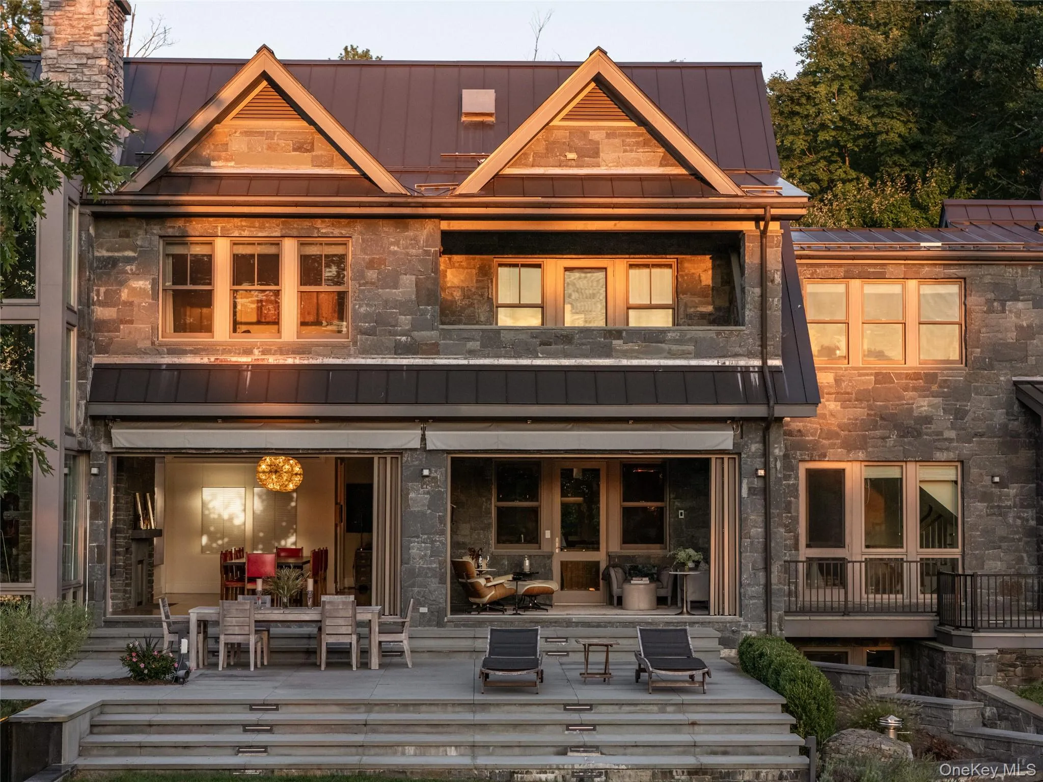 Back of property featuring a standing seam roof, a metal roof, stone siding, and a balcony Back of property featuring a standing seam roof, a metal roof, stone siding, and a balcony