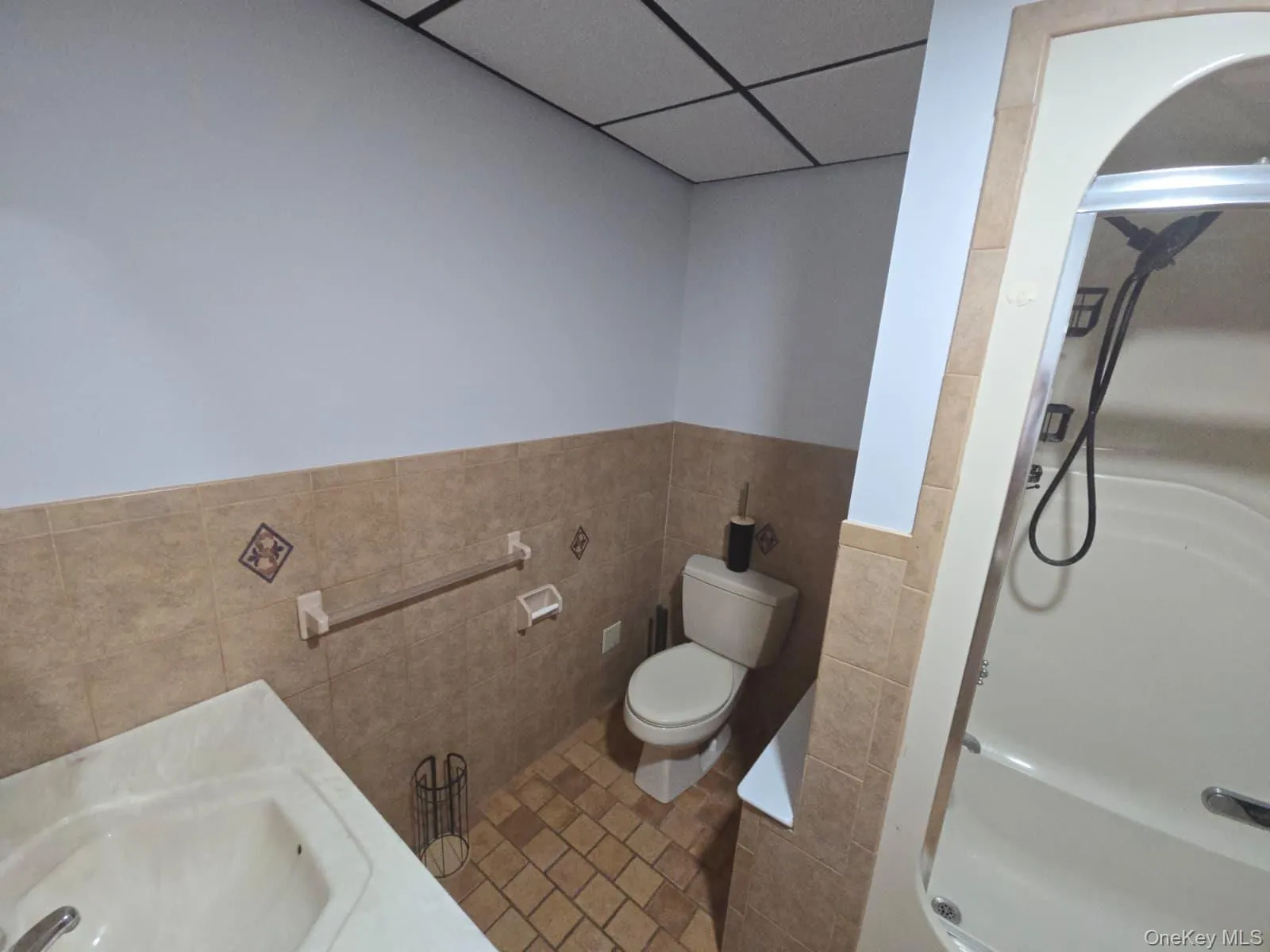 Full bathroom featuring a shower stall, tile walls, wainscoting, a paneled ceiling, and tile patterned flooring Full bathroom featuring a shower stall, tile walls, wainscoting, a paneled ceiling, and tile patterned flooring