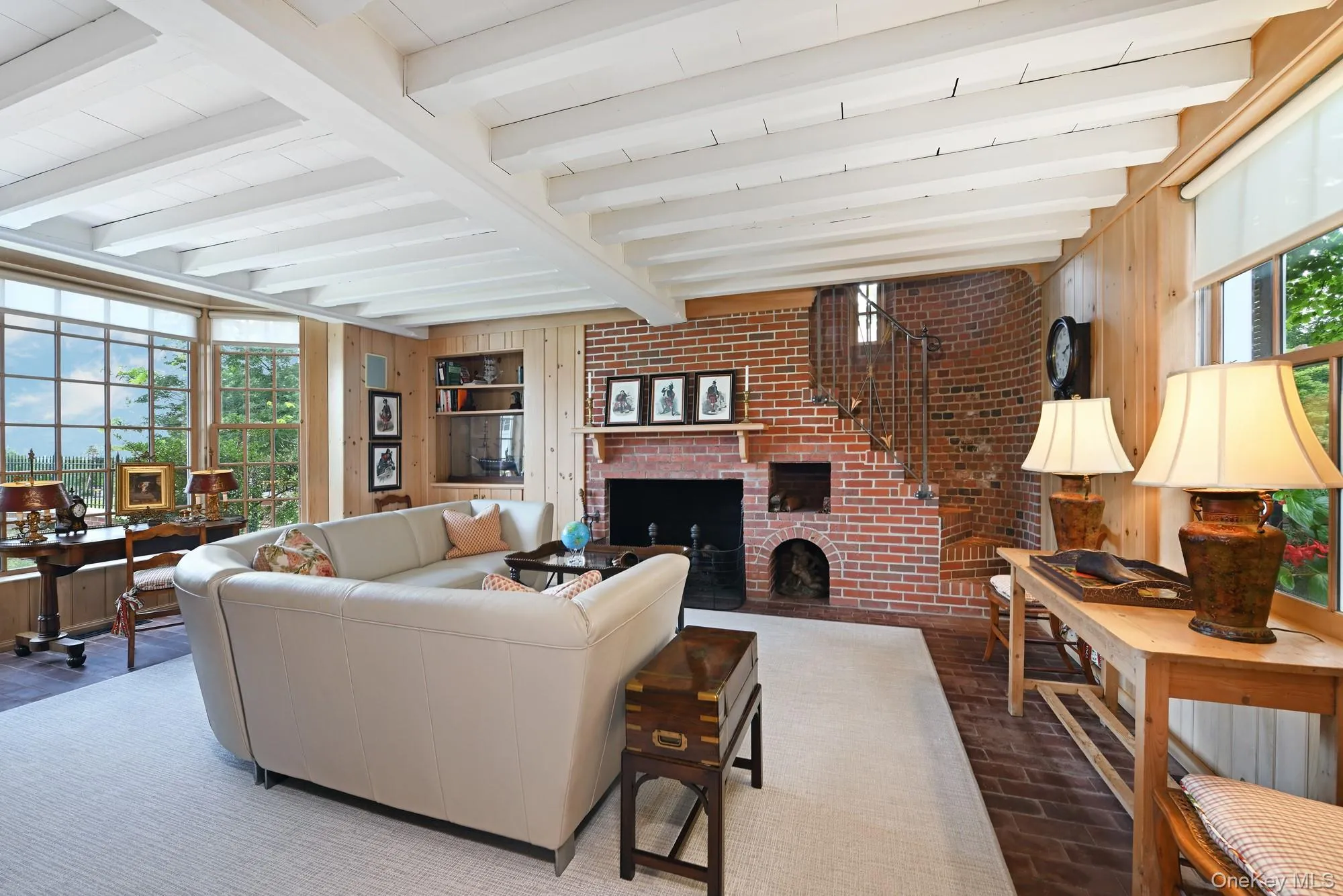 Living room featuring beam ceiling, brick flooring, a brick fireplace, wooden walls, and brick wall Living room featuring beam ceiling, brick flooring, a brick fireplace, wooden walls, and brick wall