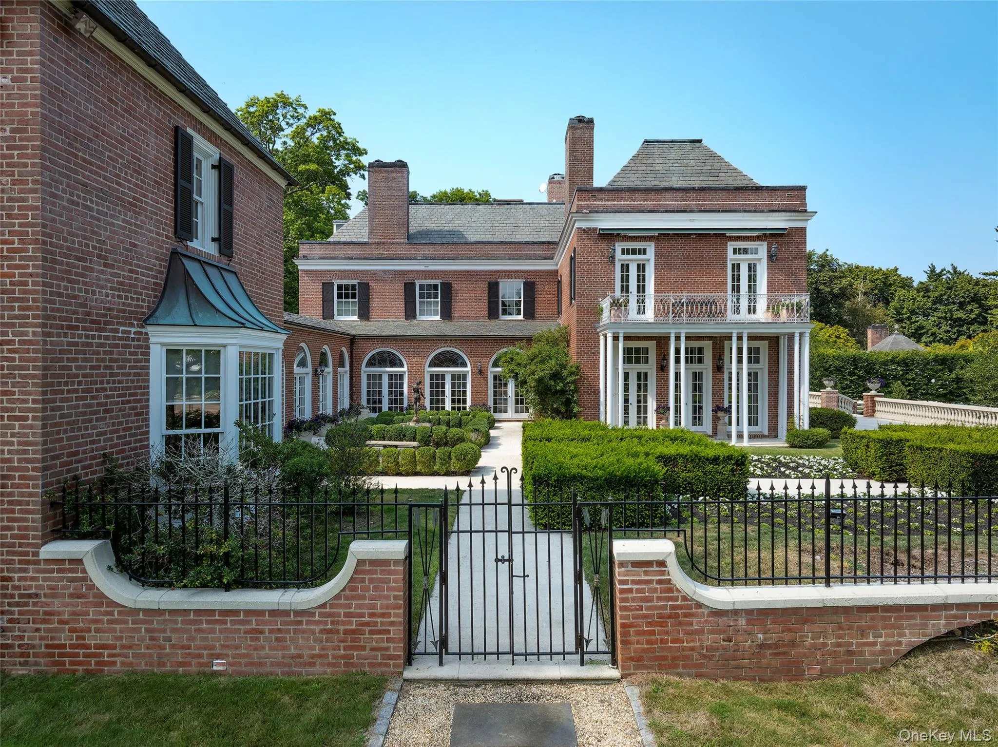 Colonial-style house featuring a gate, a fenced front yard, brick siding, and french doors Colonial-style house featuring a gate, a fenced front yard, brick siding, and french doors