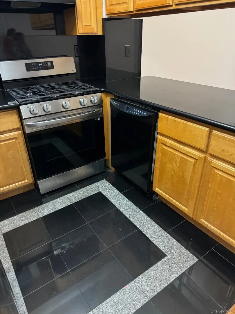 Kitchen with stainless steel gas range, dishwasher, exhaust hood, and dark tile patterned flooring Kitchen with stainless steel gas range, dishwasher, exhaust hood, and dark tile patterned flooring