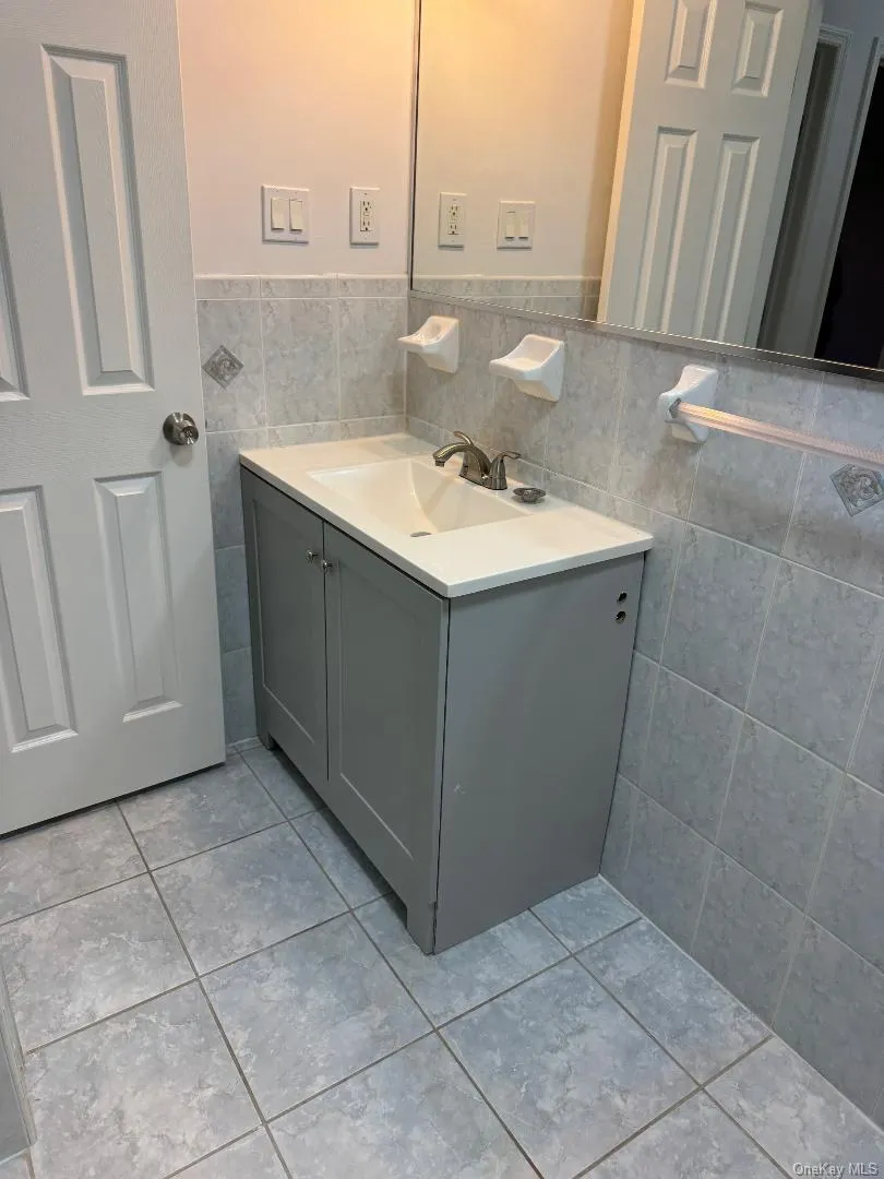 Bathroom with tile walls, vanity, light tile patterned flooring, and wainscoting Bathroom with tile walls, vanity, light tile patterned flooring, and wainscoting