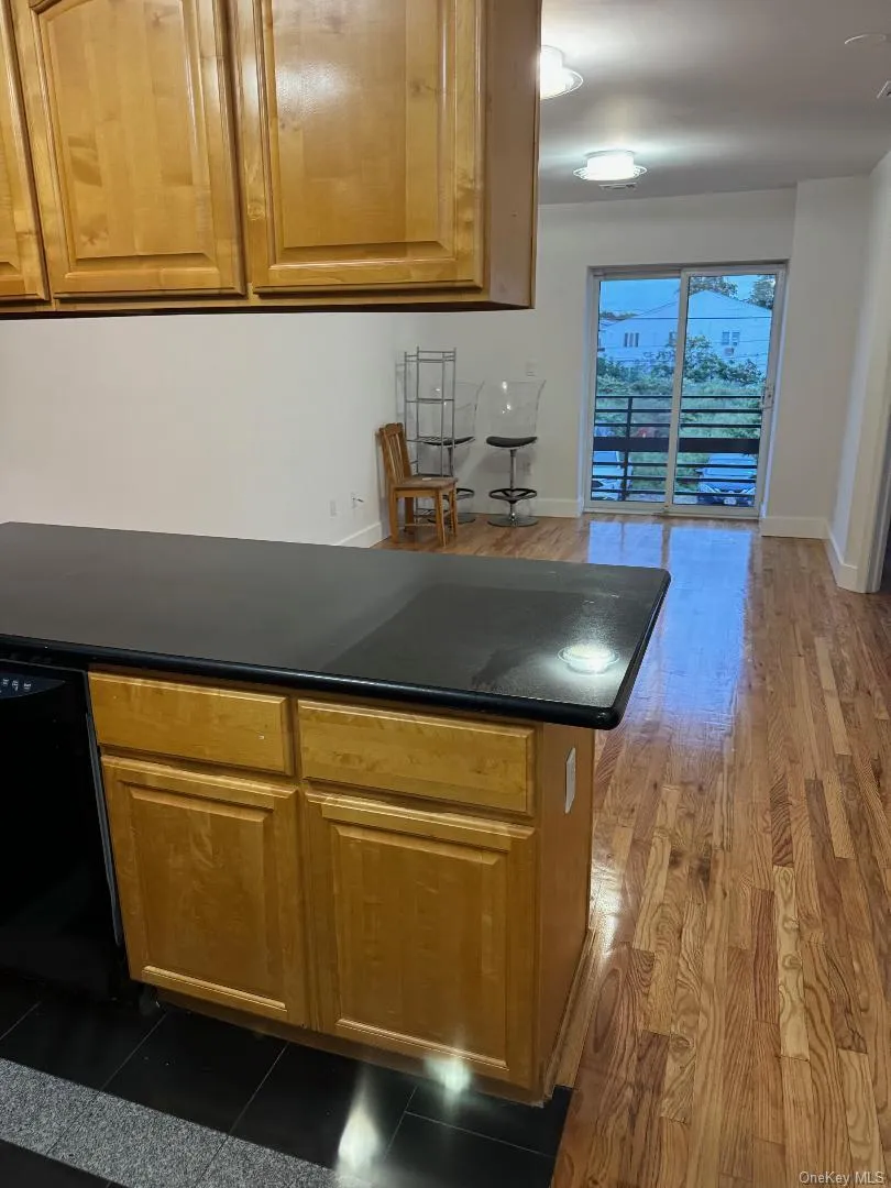 Kitchen featuring dark countertops, brown cabinetry, black dishwasher, and dark wood-style flooring Kitchen featuring dark countertops, brown cabinetry, black dishwasher, and dark wood-style flooring