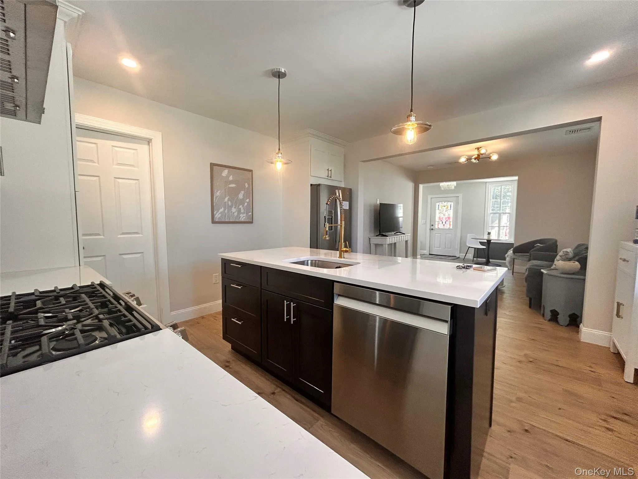 Kitchen with stainless steel appliances, hanging light fixtures, light wood-type flooring, open floor plan, and light stone countertops Kitchen with stainless steel appliances, hanging light fixtures, light wood-type flooring, open floor plan, and light stone countertops