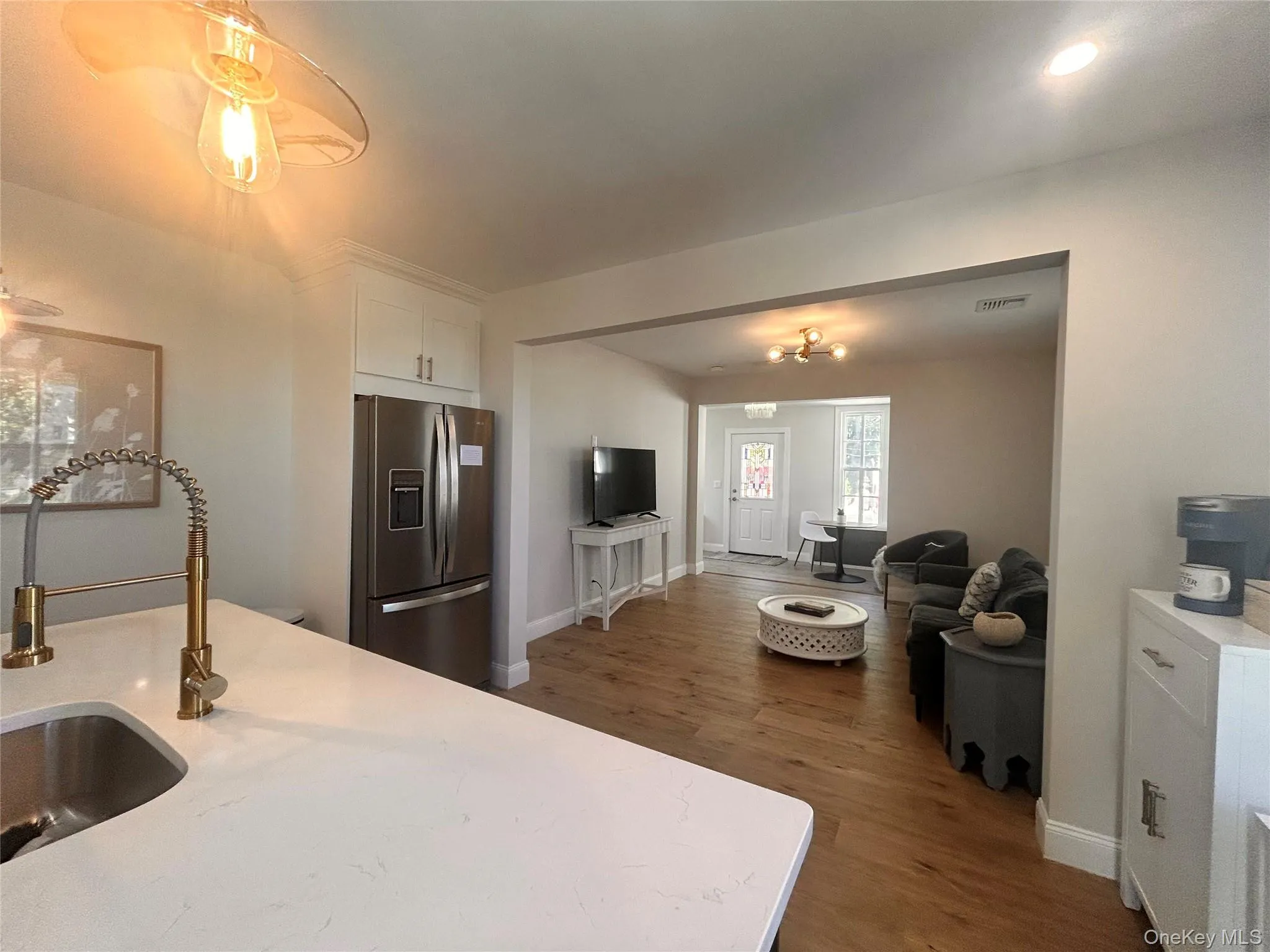 Kitchen featuring stainless steel fridge, dark wood-style flooring, white cabinetry, open floor plan, and light stone countertops Kitchen featuring stainless steel fridge, dark wood-style flooring, white cabinetry, open floor plan, and light stone countertops