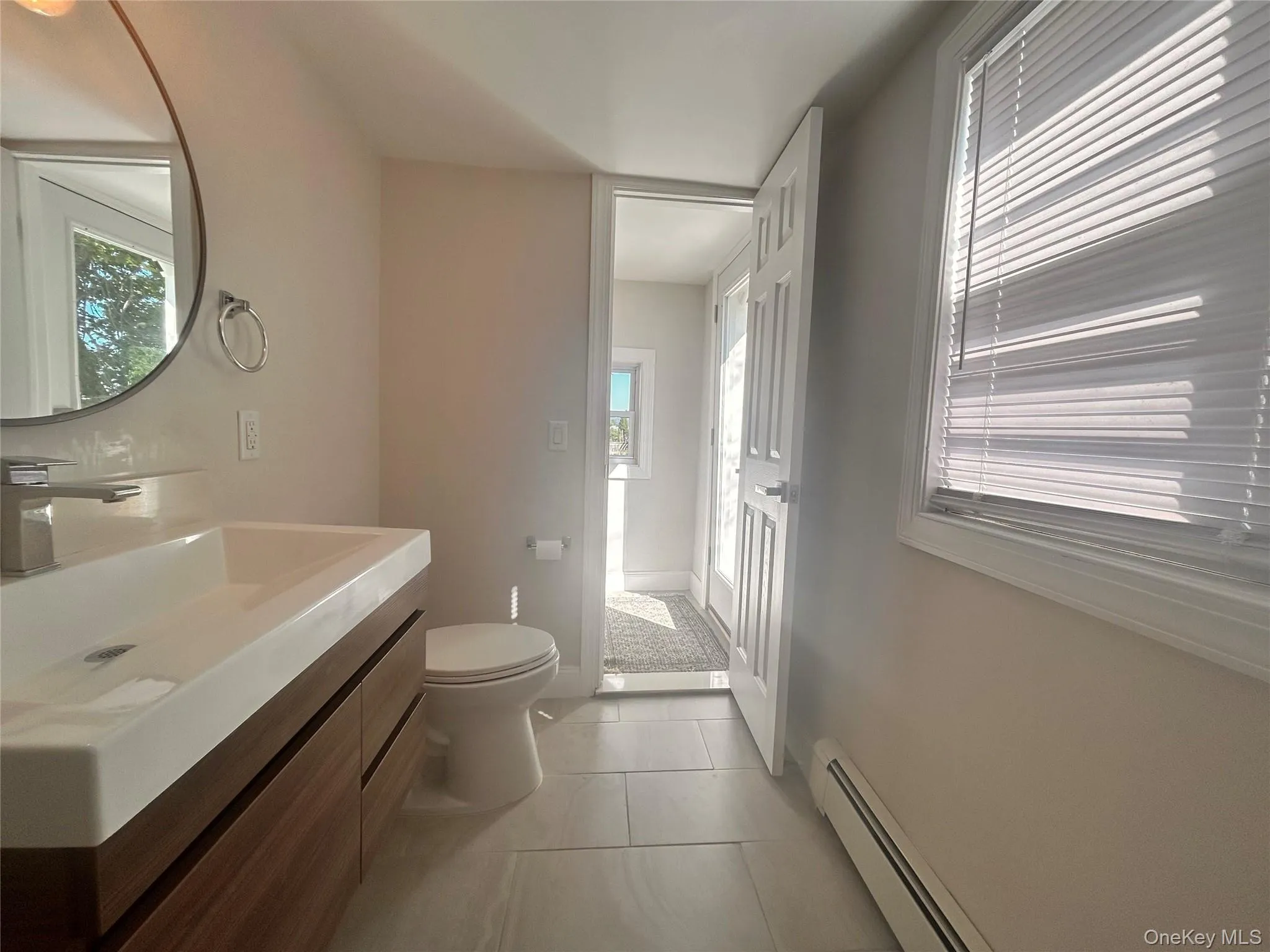 Half bath featuring a baseboard radiator, vanity, and light tile patterned flooring Half bath featuring a baseboard radiator, vanity, and light tile patterned flooring