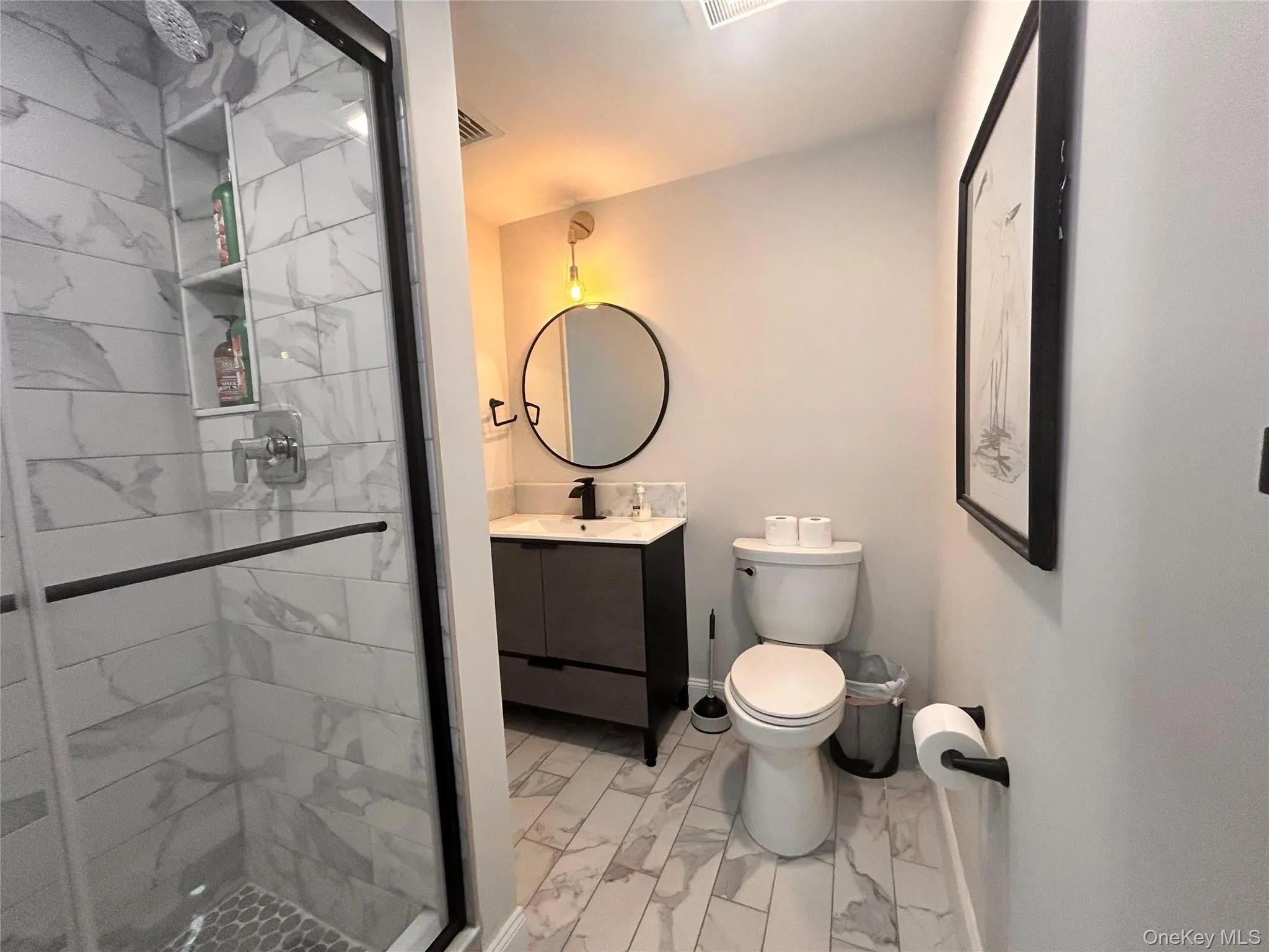 Bathroom featuring a shower stall, vanity, and light marble finish floors Bathroom featuring a shower stall, vanity, and light marble finish floors