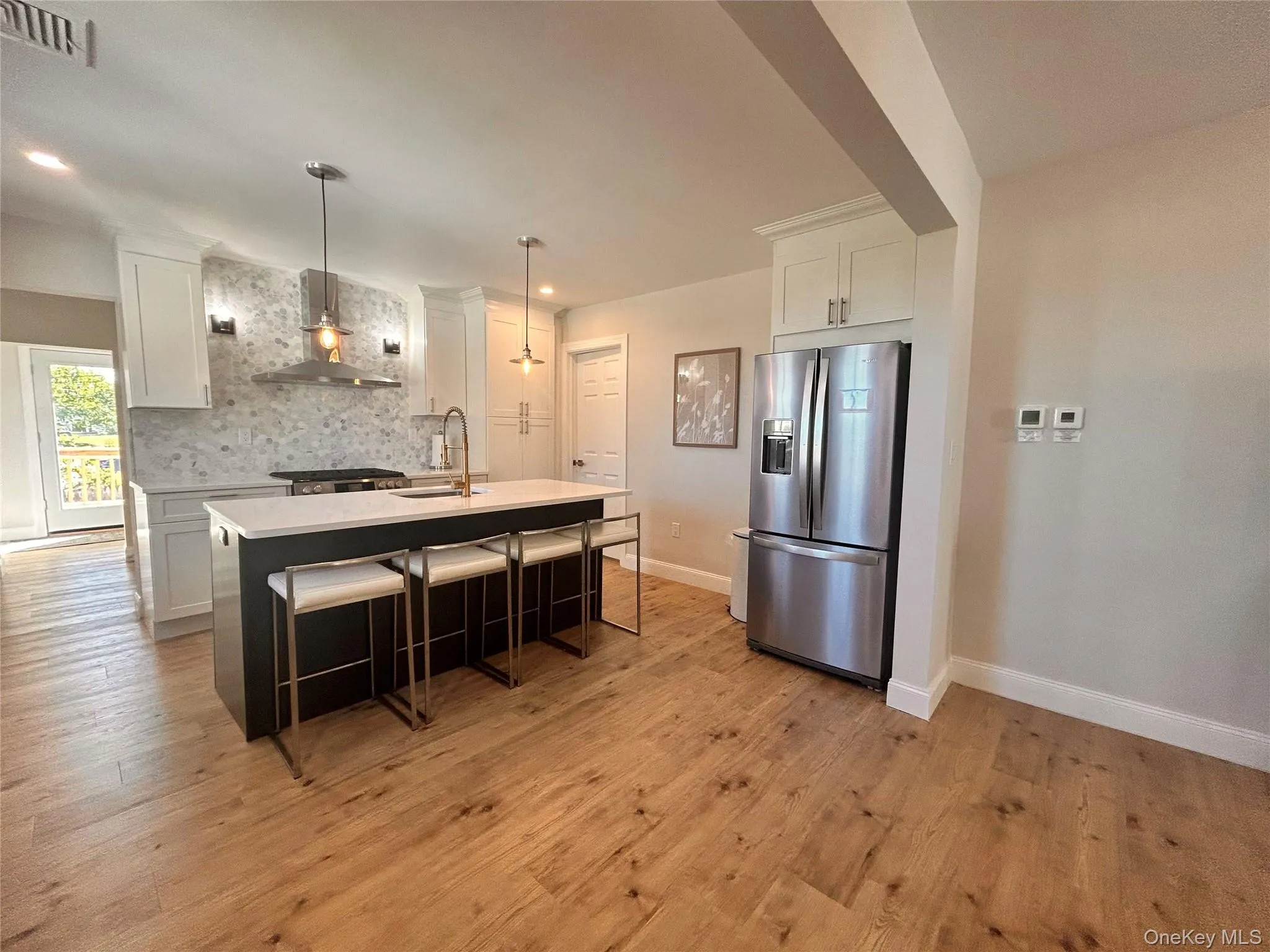 Kitchen featuring stainless steel fridge, a breakfast bar area, decorative light fixtures, wall chimney range hood, and tasteful backsplash Kitchen featuring stainless steel fridge, a breakfast bar area, decorative light fixtures, wall chimney range hood, and tasteful backsplash