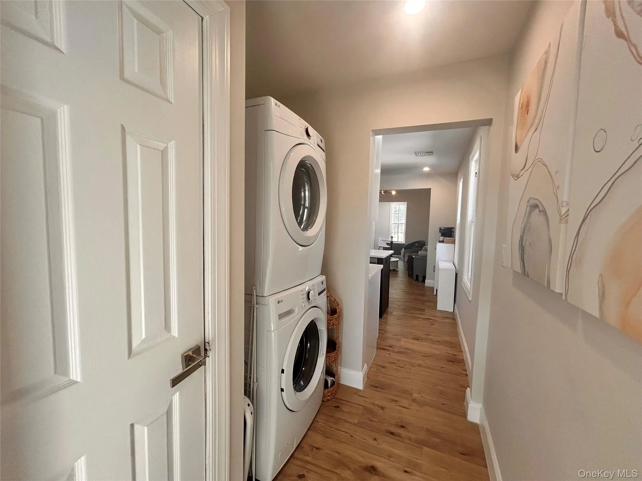 Washroom with light wood-style floors, stacked washer and clothes dryer, and recessed lighting Washroom with light wood-style floors, stacked washer and clothes dryer, and recessed lighting