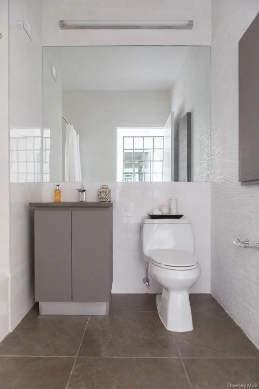 Full bath featuring tile walls, tile patterned flooring, vanity, and curtained shower Full bath featuring tile walls, tile patterned flooring, vanity, and curtained shower