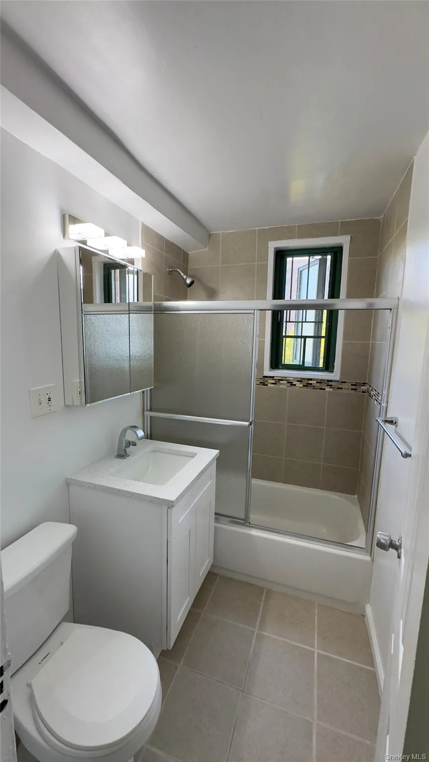 Full bathroom featuring shower / bath combination with glass door, light tile patterned flooring, and vanity Full bathroom featuring shower / bath combination with glass door, light tile patterned flooring, and vanity