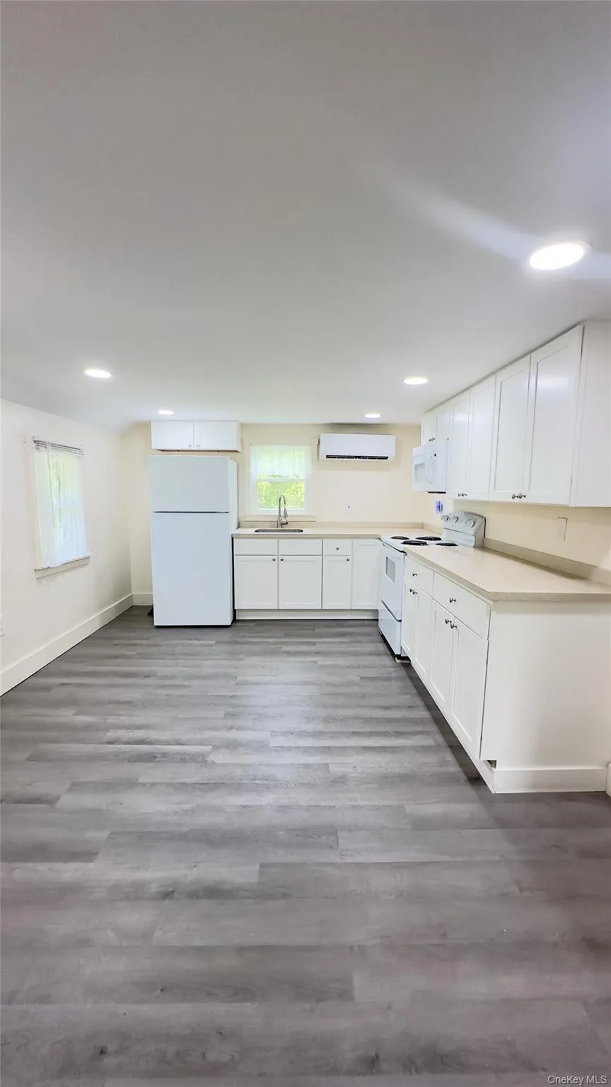 Kitchen with white appliances, white cabinets, a wall mounted air conditioner, vinyl floors, and recessed lighting Kitchen with white appliances, white cabinets, a wall mounted air conditioner, vinyl floors, and recessed lighting