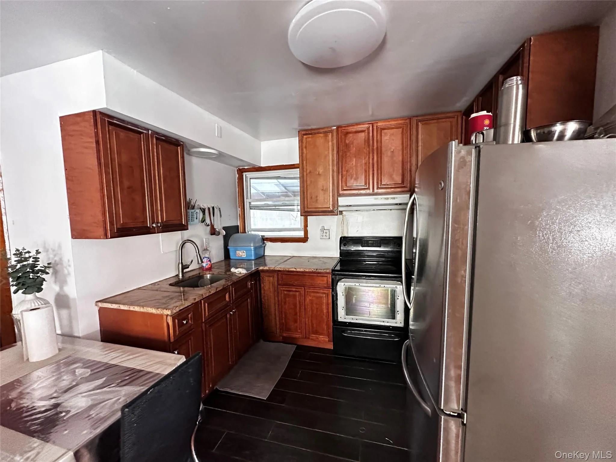 Kitchen with freestanding refrigerator, black range with electric cooktop, brown cabinets, and under cabinet range hood Kitchen with freestanding refrigerator, black range with electric cooktop, brown cabinets, and under cabinet range hood