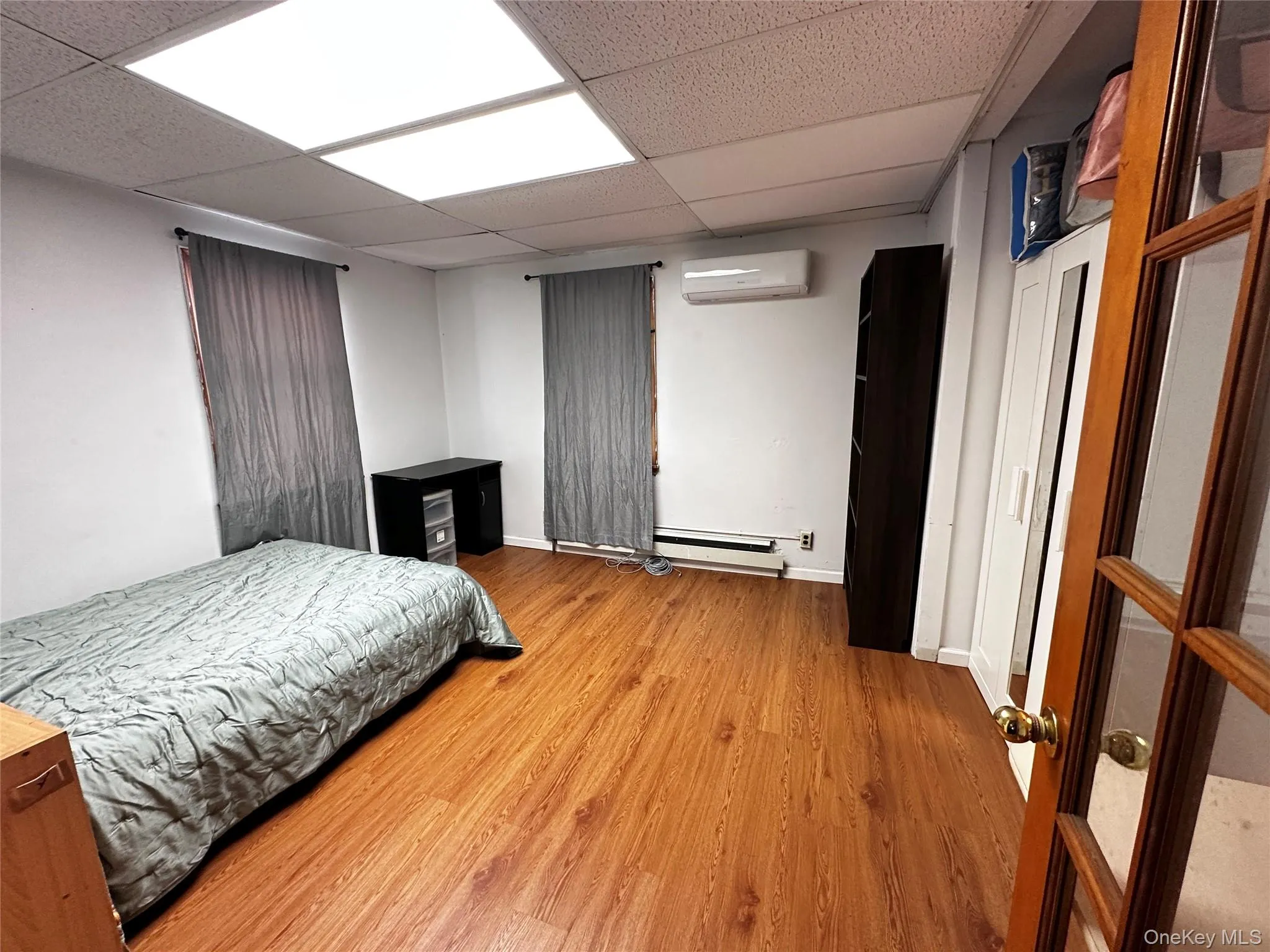 Bedroom with light wood finished floors, a drop ceiling, a baseboard heating unit, and a wall unit AC Bedroom with light wood finished floors, a drop ceiling, a baseboard heating unit, and a wall unit AC