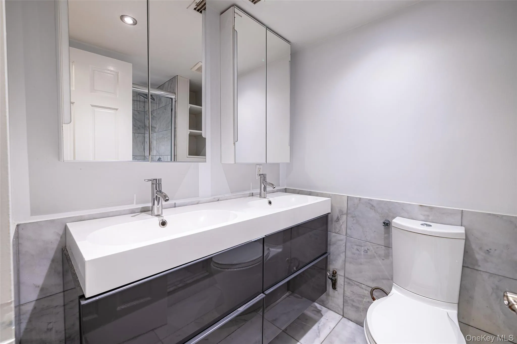 Bathroom featuring double vanity, tile walls, wainscoting, and recessed lighting Bathroom featuring double vanity, tile walls, wainscoting, and recessed lighting