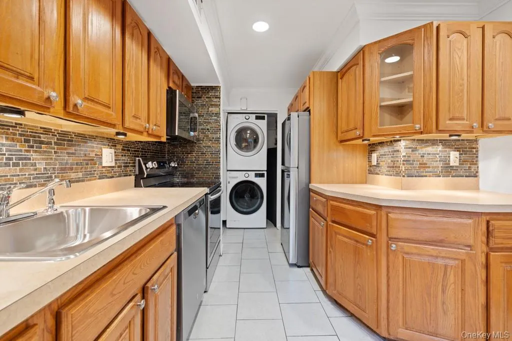 Kitchen with decorative backsplash, brown cabinets, appliances with stainless steel finishes, light tile patterned flooring, and light countertops Kitchen with decorative backsplash, brown cabinets, appliances with stainless steel finishes, light tile patterned flooring, and light countertops