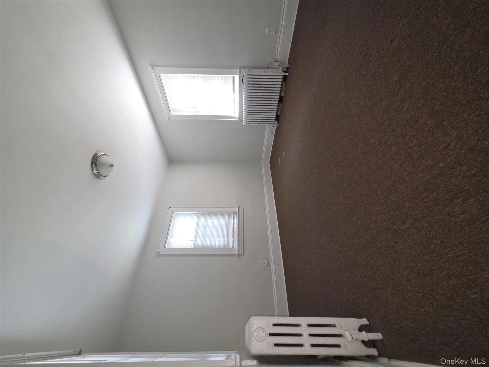Empty room featuring radiator heating unit and dark colored carpet Empty room featuring radiator heating unit and dark colored carpet