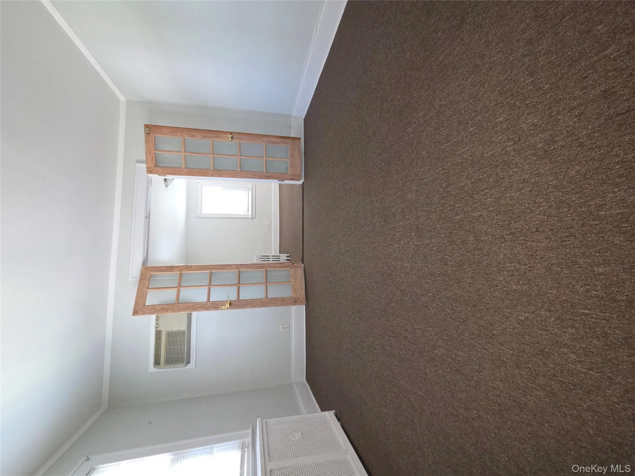 Unfurnished room featuring dark colored carpet, french doors, radiator, ornamental molding, and a wall mounted air conditioner Unfurnished room featuring dark colored carpet, french doors, radiator, ornamental molding, and a wall mounted air conditioner