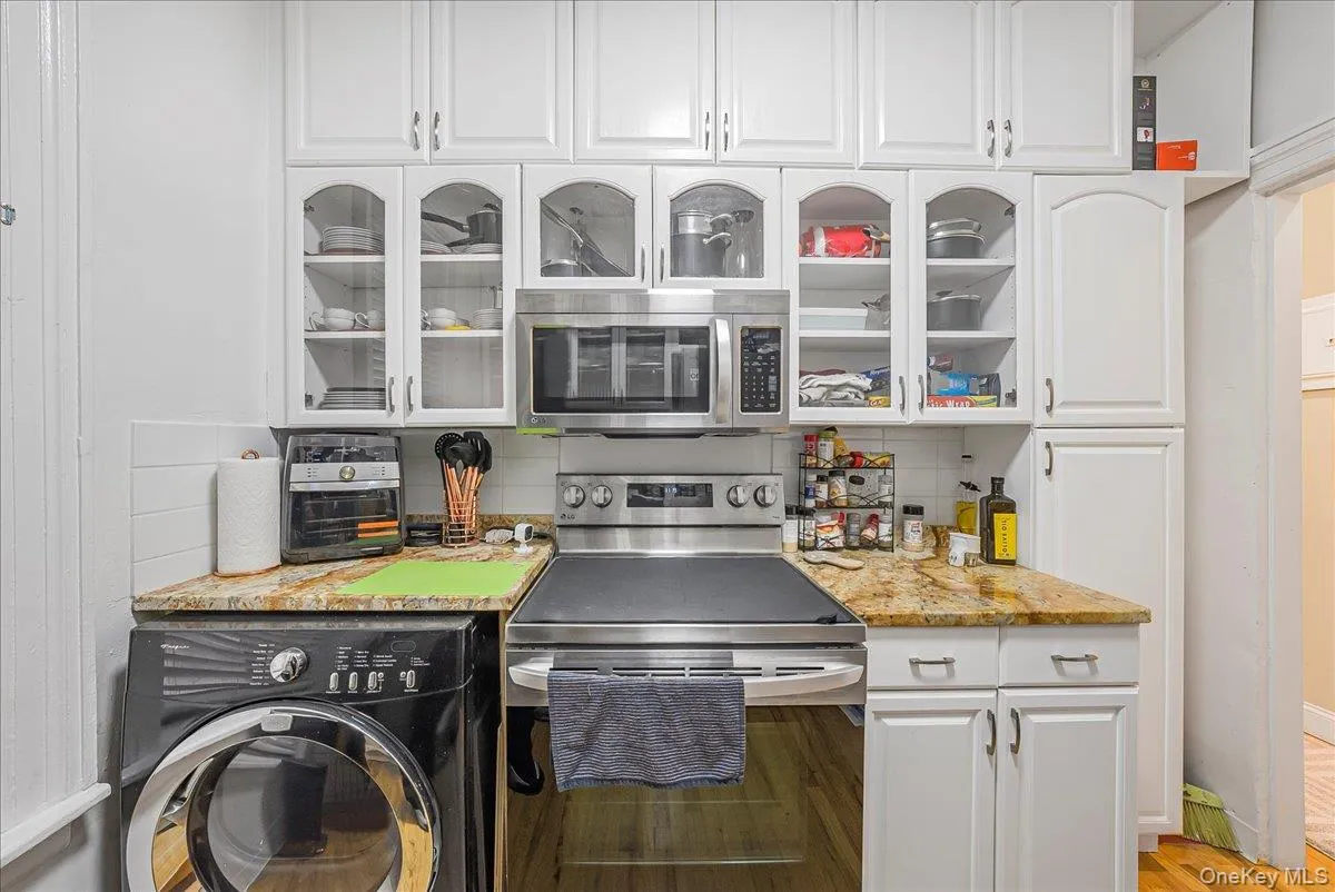 Kitchen with stainless steel appliances, white cabinets, washer / dryer, light stone countertops, and backsplash Kitchen with stainless steel appliances, white cabinets, washer / dryer, light stone countertops, and backsplash