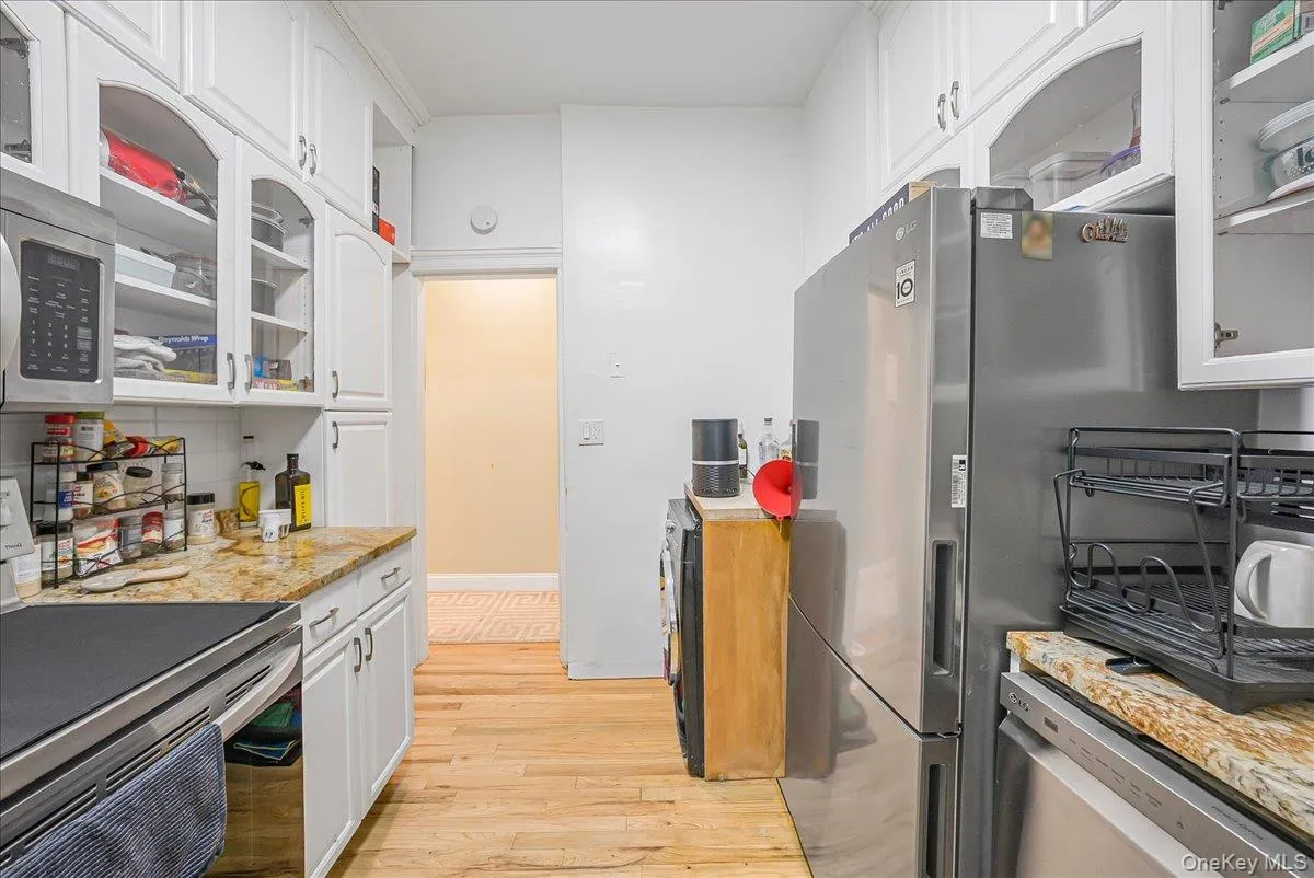 Kitchen with glass insert cabinets, appliances with stainless steel finishes, white cabinets, light stone counters, and light wood finished floors Kitchen with glass insert cabinets, appliances with stainless steel finishes, white cabinets, light stone counters, and light wood finished floors