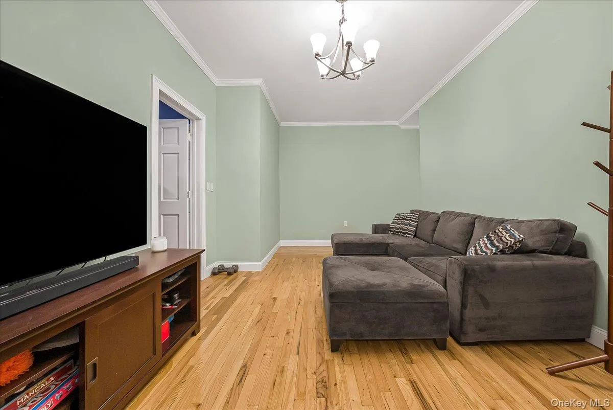 Living area with light wood finished floors, ornamental molding, and a chandelier Living area with light wood finished floors, ornamental molding, and a chandelier