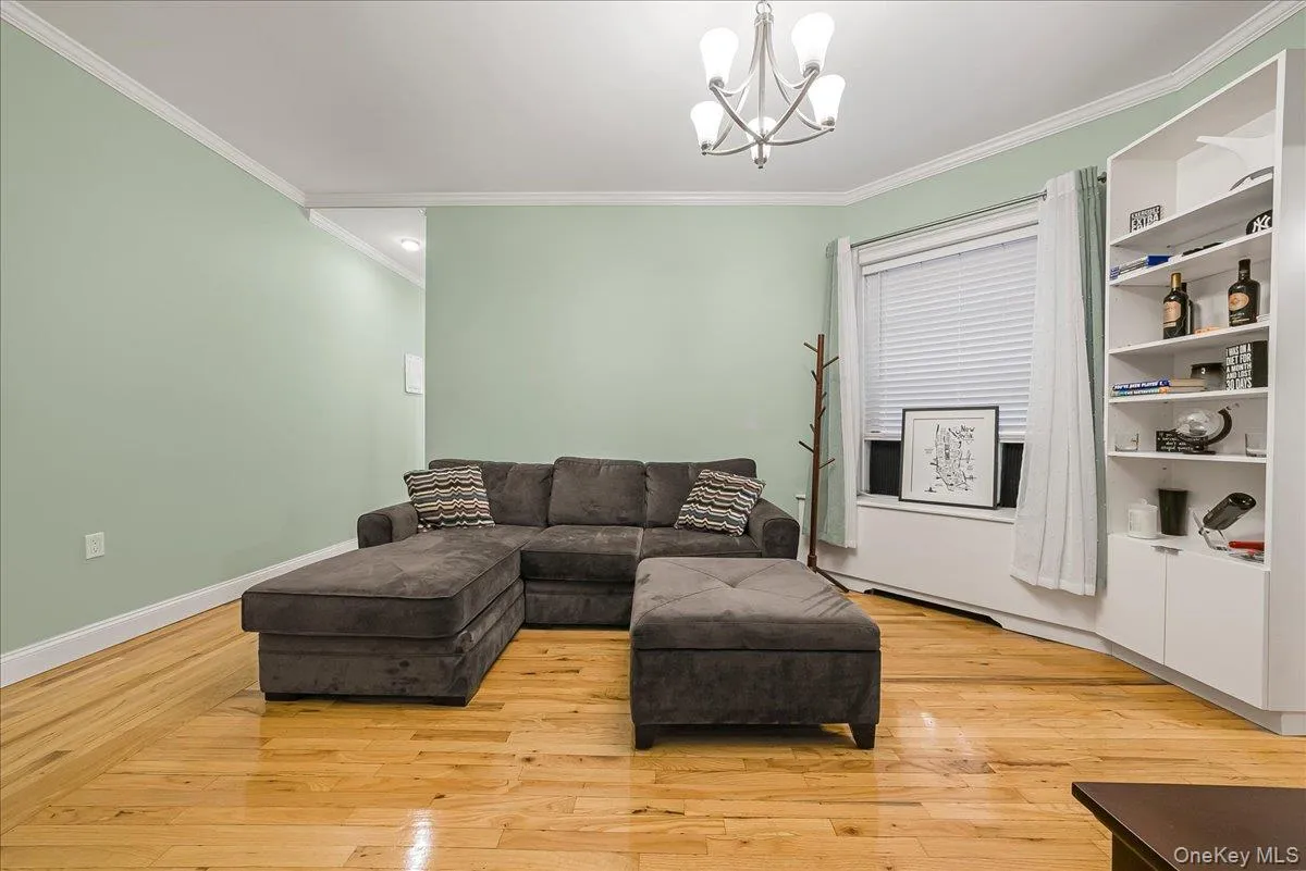 Living room featuring ornamental molding, light wood-style floors, and a chandelier Living room featuring ornamental molding, light wood-style floors, and a chandelier