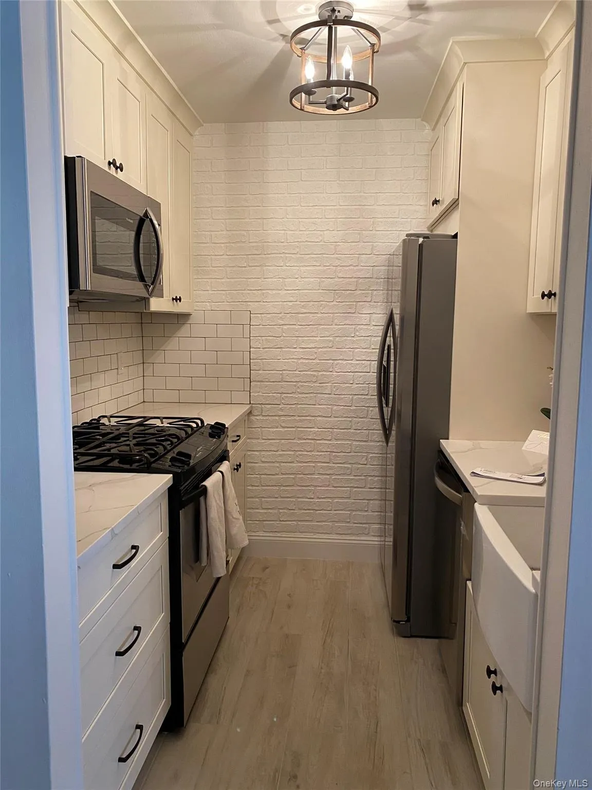 Kitchen featuring white cabinets, stainless steel appliances, light wood-style floors, and light stone counters Kitchen featuring white cabinets, stainless steel appliances, light wood-style floors, and light stone counters
