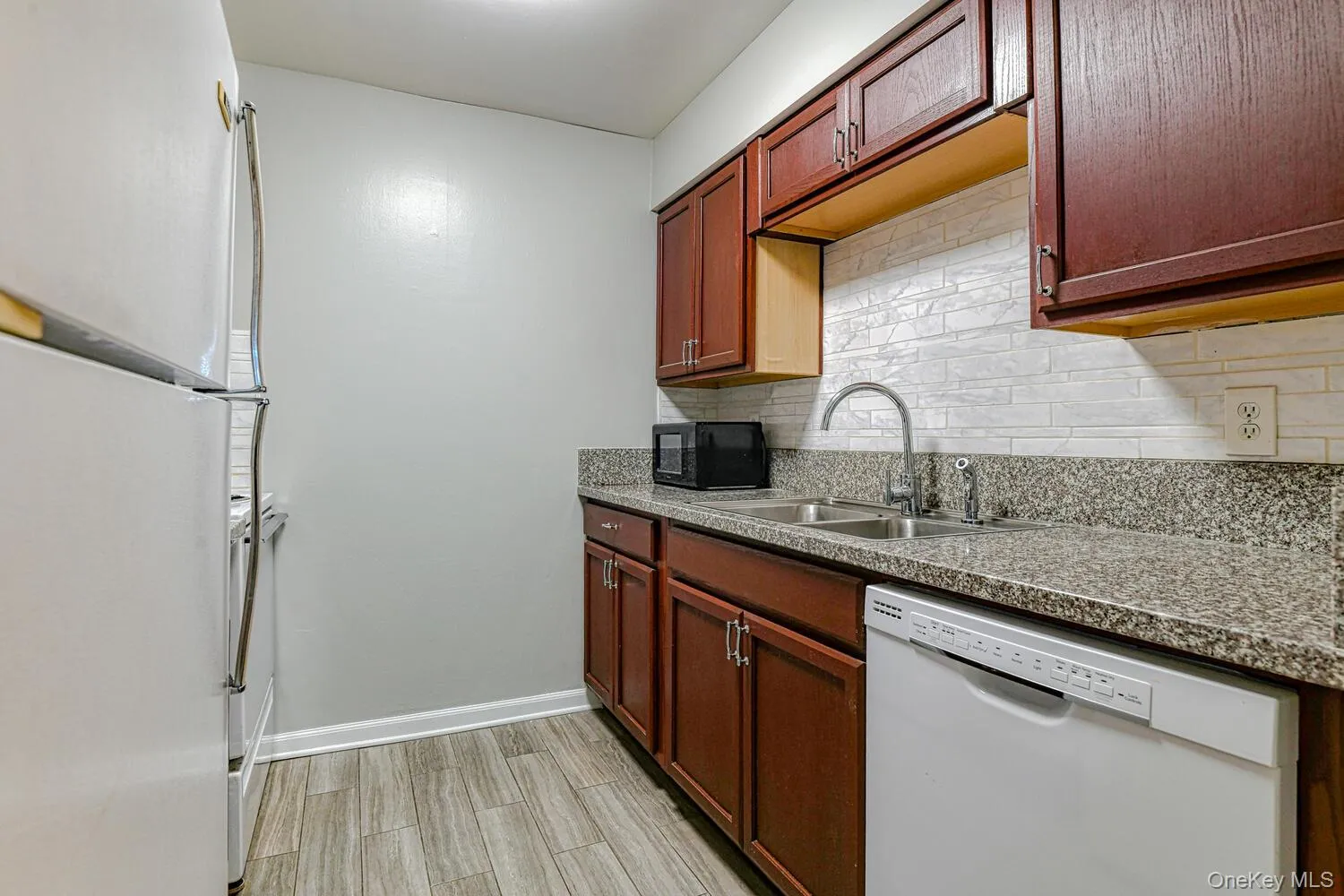 Kitchen with white appliances, decorative backsplash, light wood-style flooring, and light countertops Kitchen with white appliances, decorative backsplash, light wood-style flooring, and light countertops