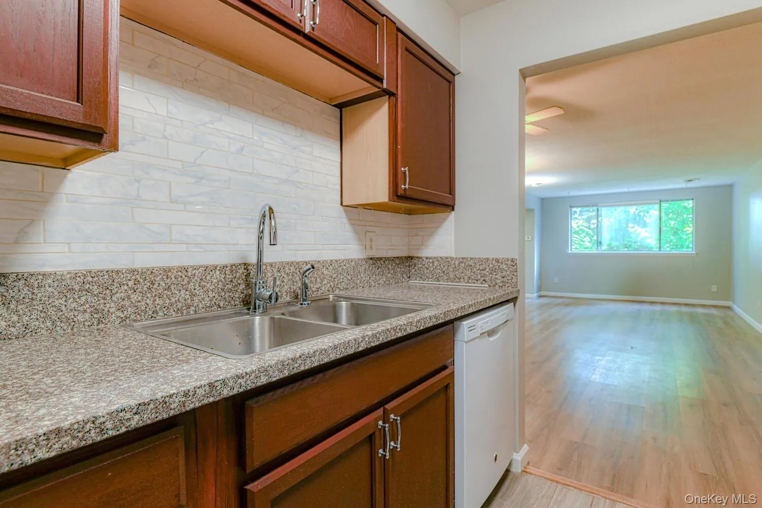 Kitchen with light wood-style floors, decorative backsplash, dishwasher, light stone countertops, and brown cabinets Kitchen with light wood-style floors, decorative backsplash, dishwasher, light stone countertops, and brown cabinets