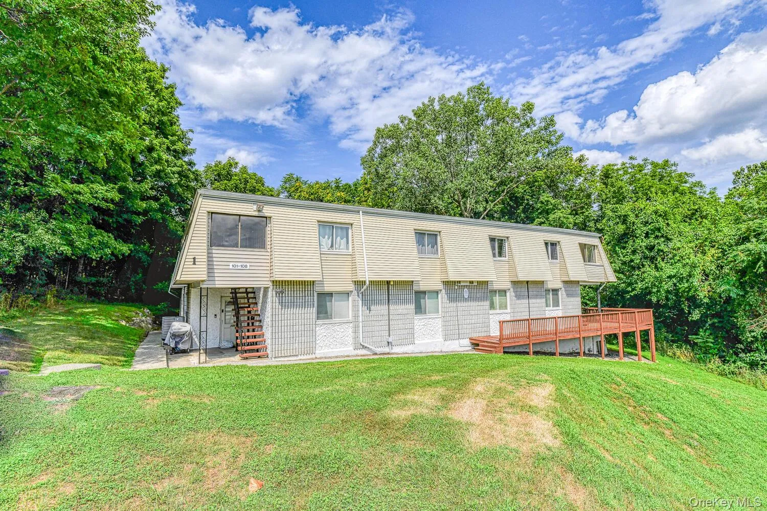 View of front of property with a deck, a front yard, stairs, and view of scattered trees View of front of property with a deck, a front yard, stairs, and view of scattered trees