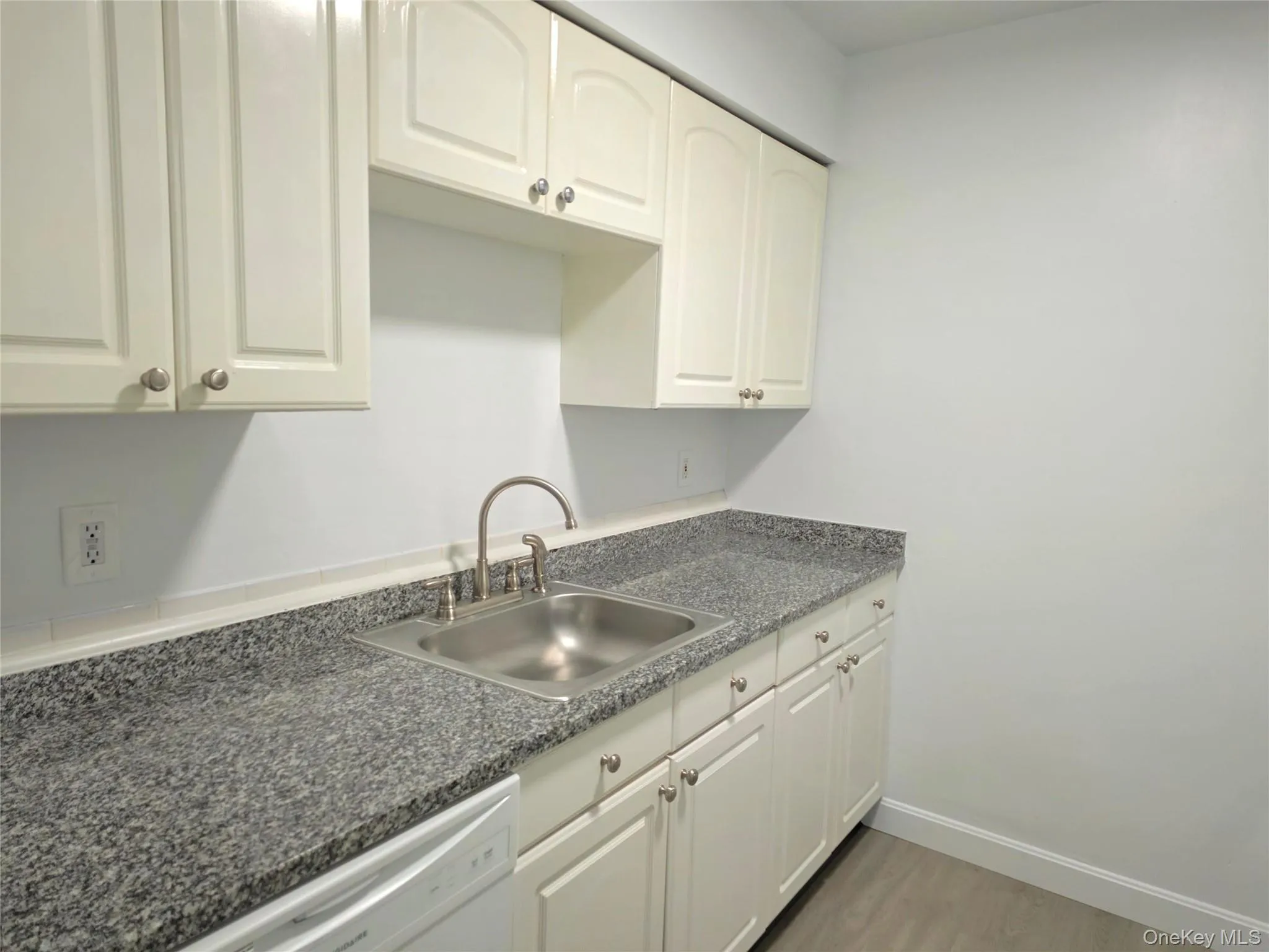 Kitchen with white dishwasher, light wood-style flooring, and white cabinets Kitchen with white dishwasher, light wood-style flooring, and white cabinets