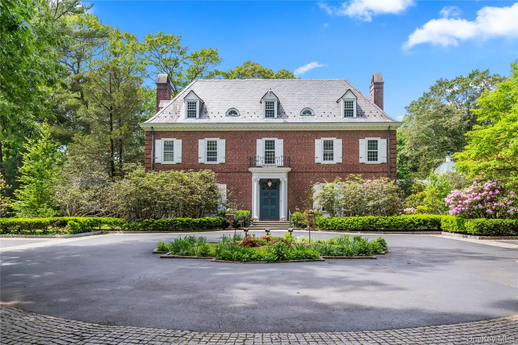 Colonial house featuring a chimney, curved driveway, brick siding, and a high end roof Colonial house featuring a chimney, curved driveway, brick siding, and a high end roof