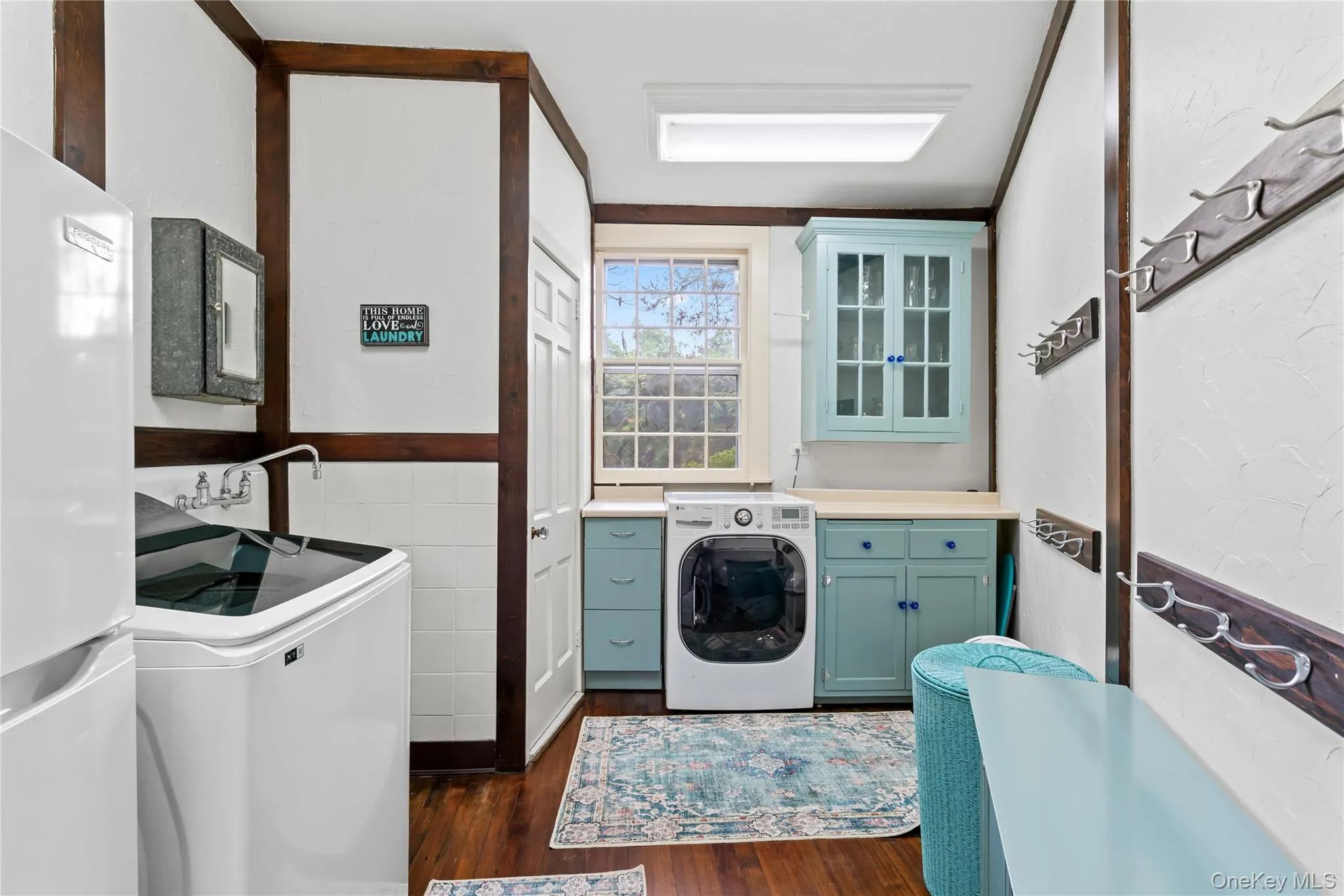 Laundry room featuring dark wood-style floors, tile walls, wainscoting, separate washer and dryer, and cabinet space Laundry room featuring dark wood-style floors, tile walls, wainscoting, separate washer and dryer, and cabinet space