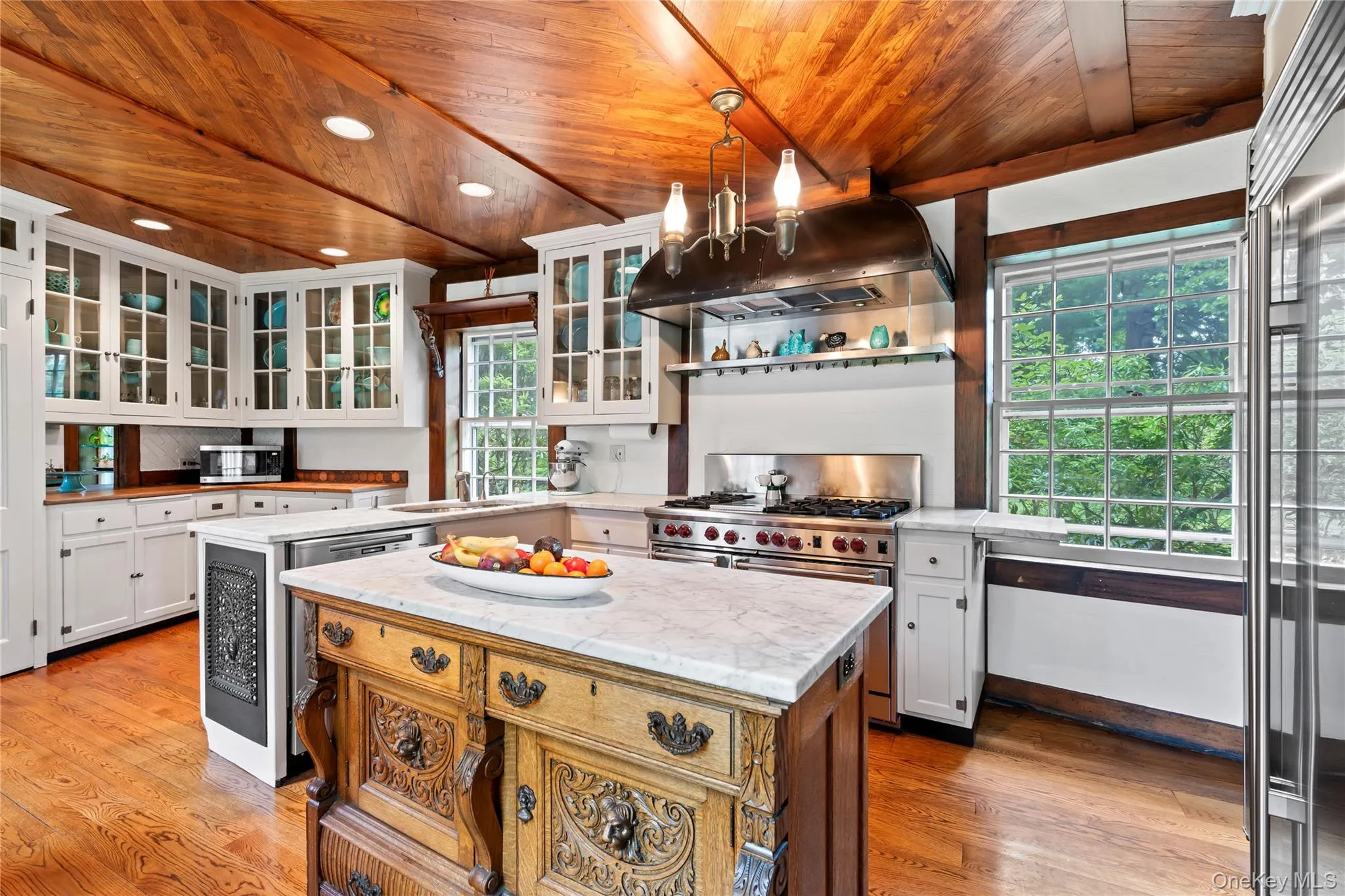 Kitchen with hanging light fixtures, white cabinets, a center island, glass insert cabinets, and under cabinet range hood Kitchen with hanging light fixtures, white cabinets, a center island, glass insert cabinets, and under cabinet range hood