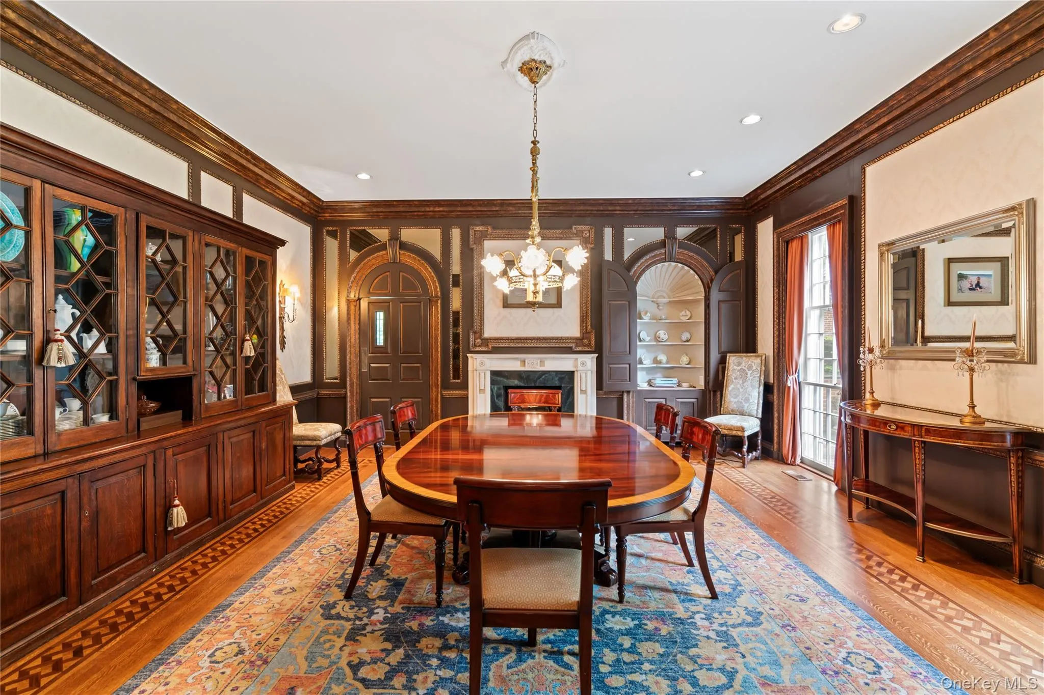 Dining room featuring crown molding, wood finished floors, a chandelier, a decorative wall, and a premium fireplace Dining room featuring crown molding, wood finished floors, a chandelier, a decorative wall, and a premium fireplace